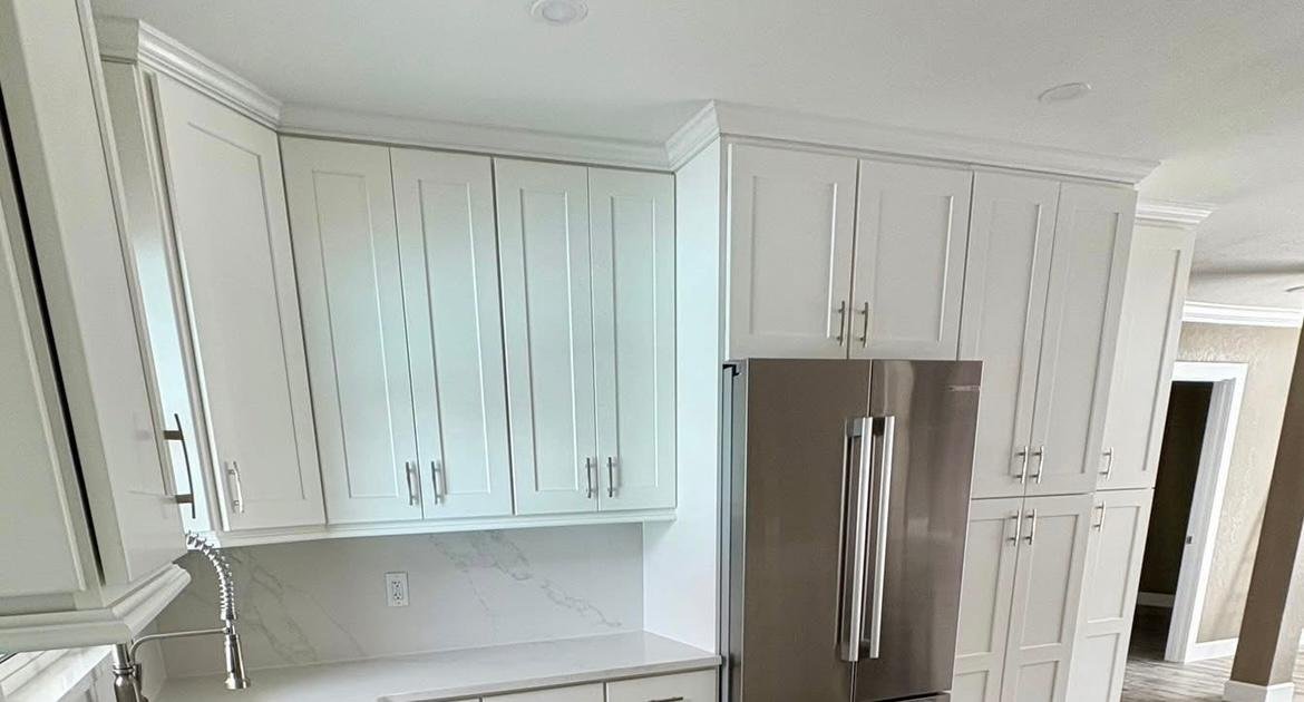 Modern kitchen with white cabinets, stainless steel refrigerator, and marble countertops.