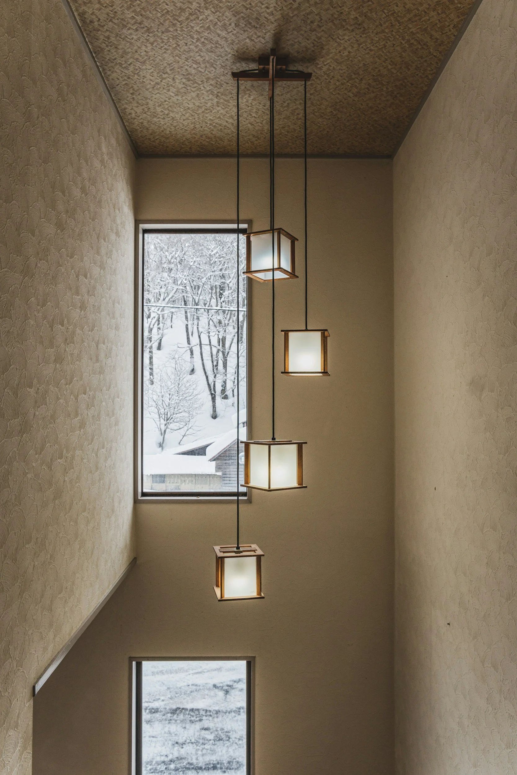 Interior view of a stairwell with hanging modern pendant lights and a large window showing a snowy landscape outside.