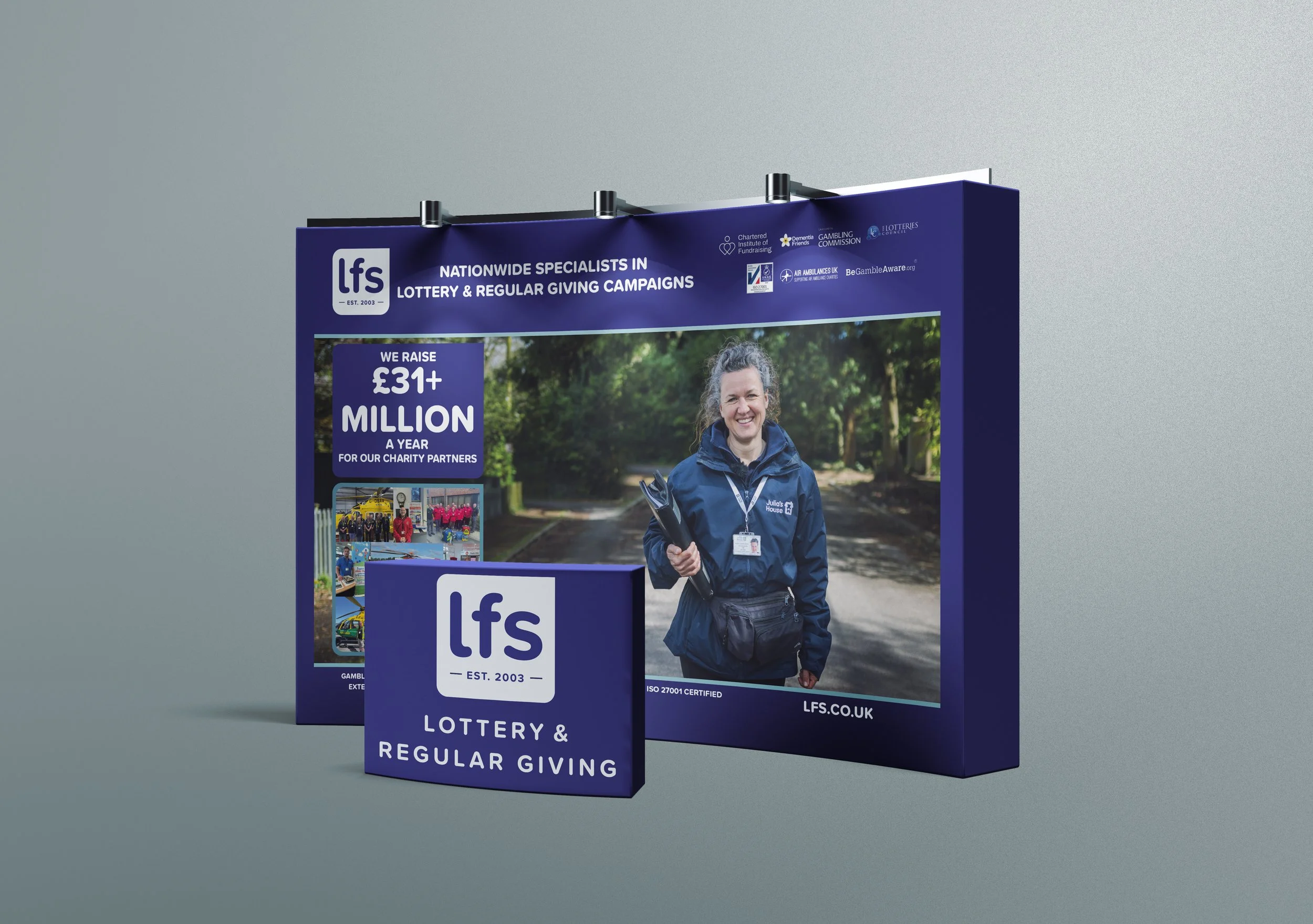A promotional display for the lottery and regular giving campaigns by LFS, featuring a smiling woman holding a clipboard, with information about raising over £31 million annually for charity partners and various logos at the top.