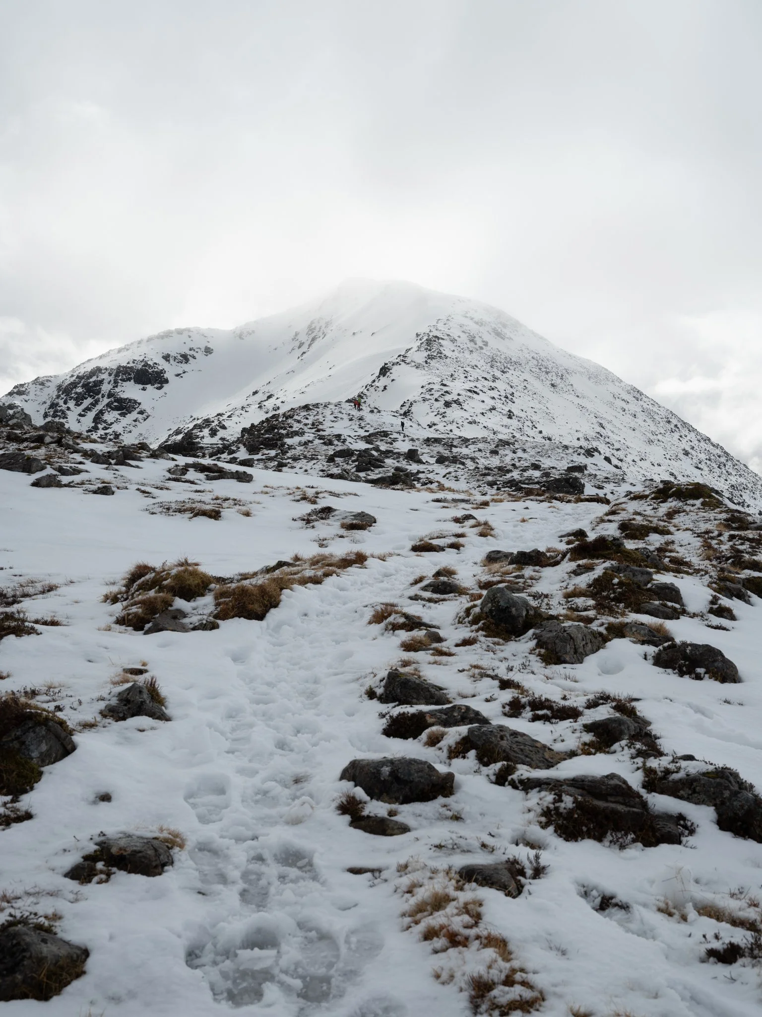 Snow-covered mountain with rocky path leading up, overcast sky.
