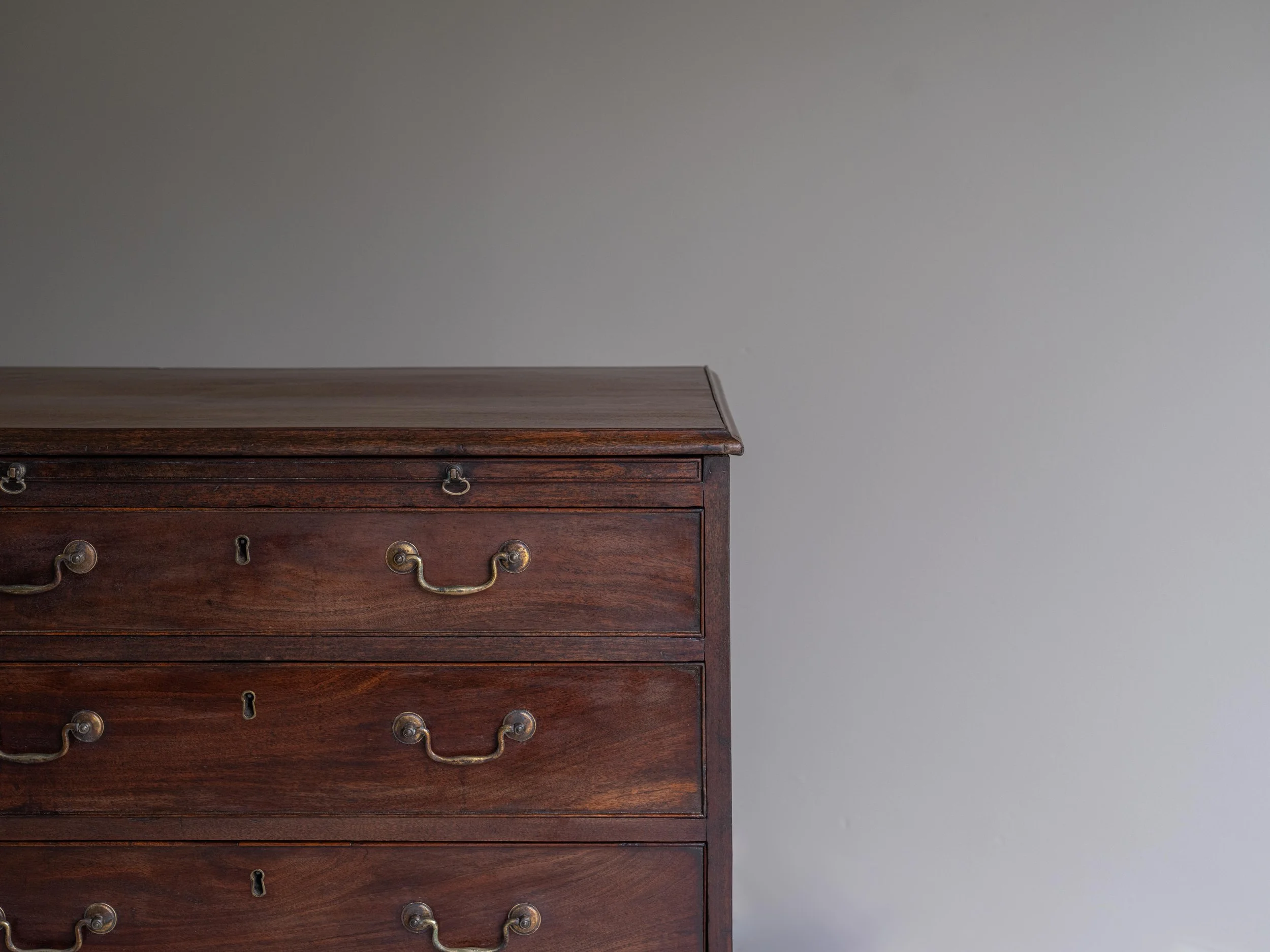 Close-up of a vintage wooden dresser with brass handles, set against a plain white wall.