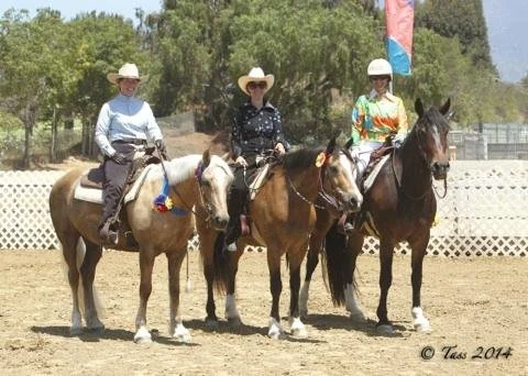 Three women wearing cowboy hats and sunglasses sitting on horses in an outdoor riding arena.