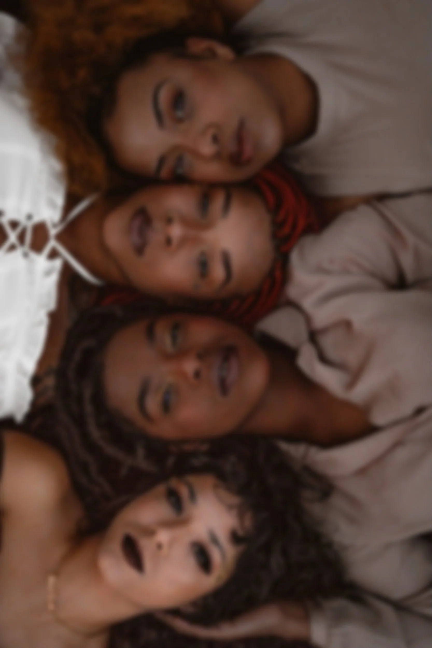 Two women with braided hair lying side by side, with faces close together, on a bed.
