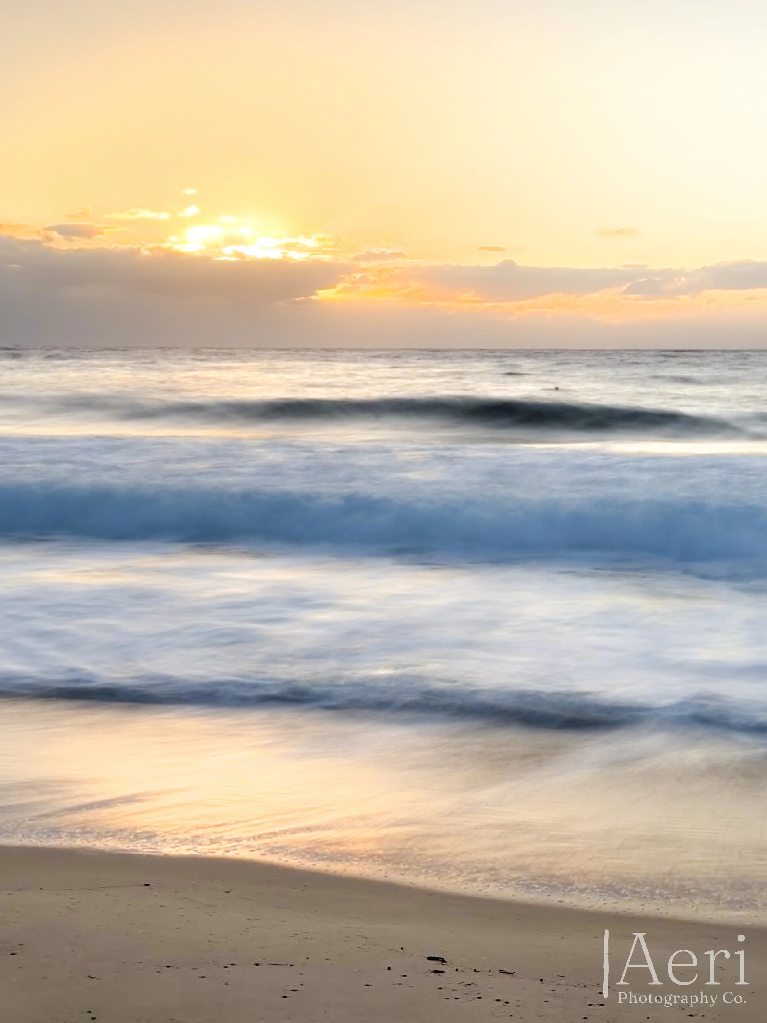 Sunset or sunrise over the ocean with waves gently crashing on the sandy beach.
