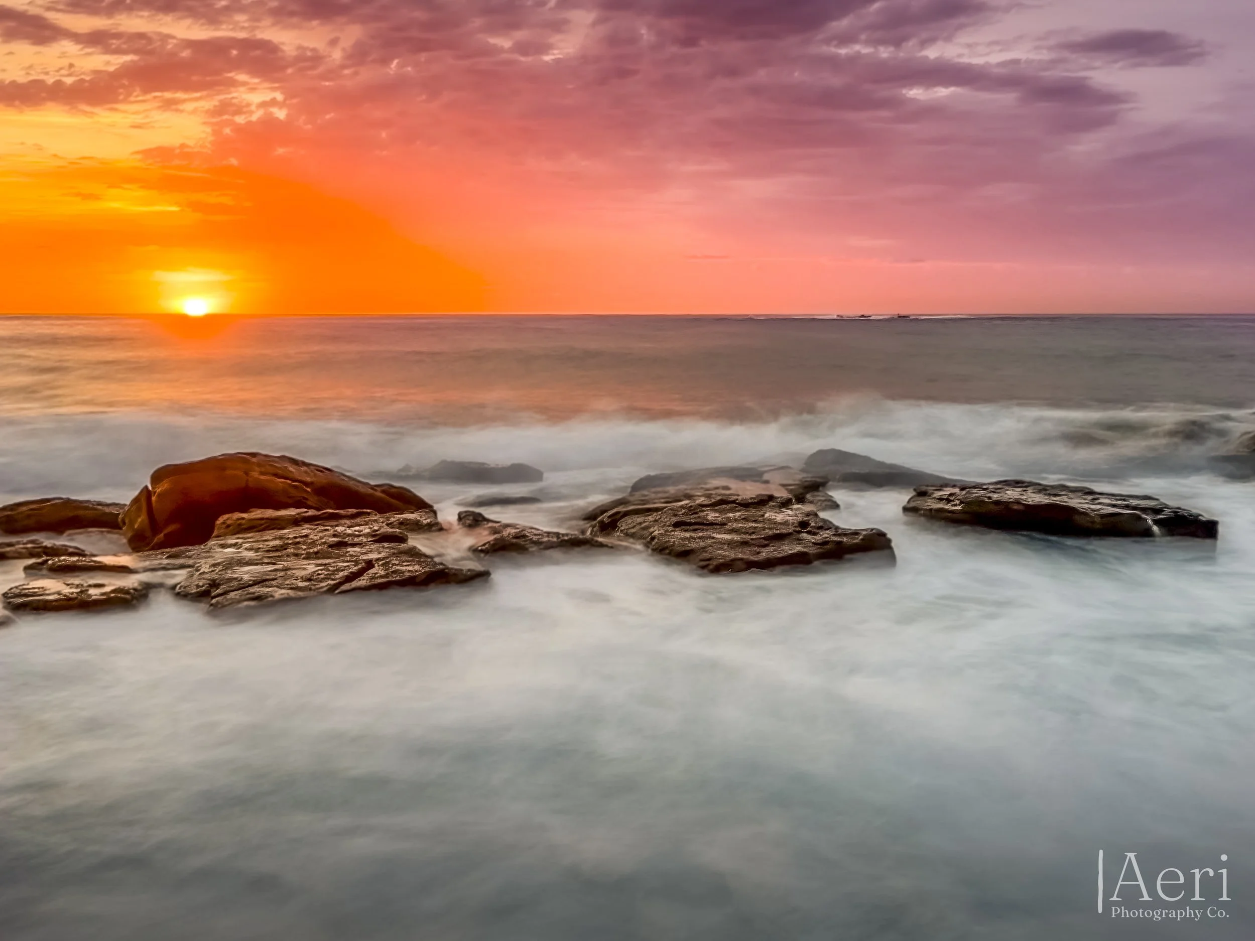 Sunset over the ocean with colorful sky and rocks in the foreground