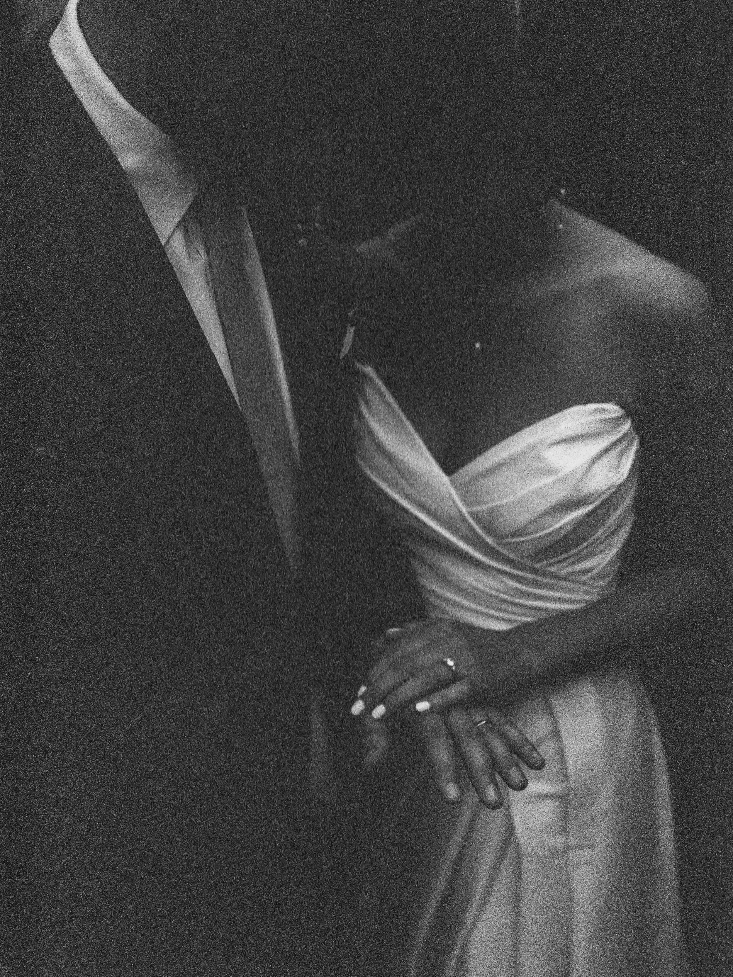 Black and white photo of a partially dressed woman sitting with her hands on her lap, wearing a striped top and pants.