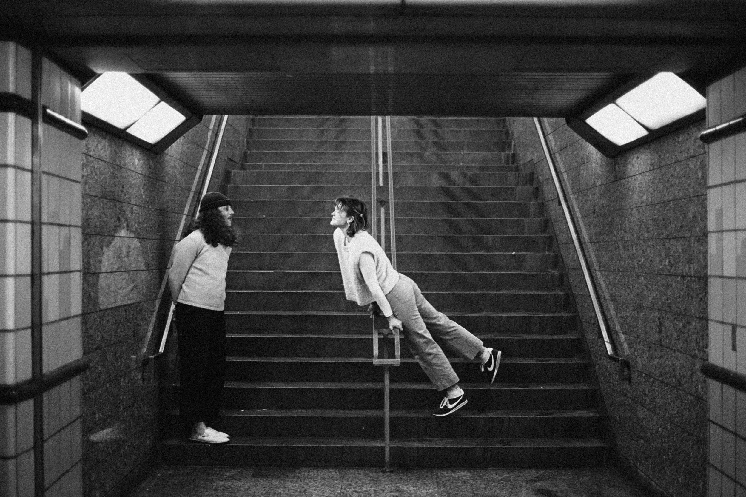 A woman leaning on a handrail and a woman standing on a staircase in an underground station.