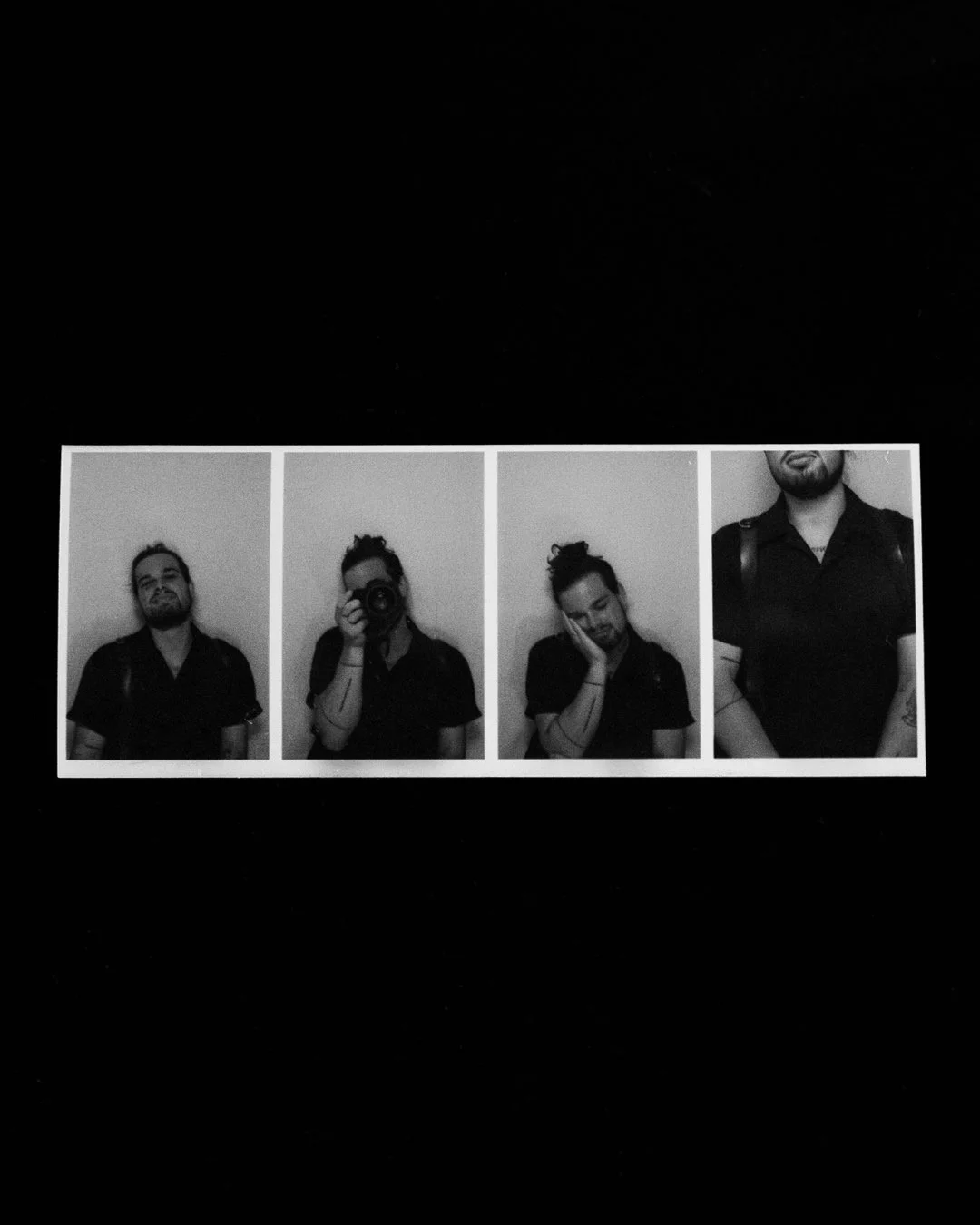 Four black and white photo booth pictures of a man with long hair tied back, wearing a black shirt. In the second photo, he is taking a picture with a camera. In the third, he resting his head on his hand with eyes closed. In the fourth, only the upper part of his body is visible, showing a tattoo on his arm.