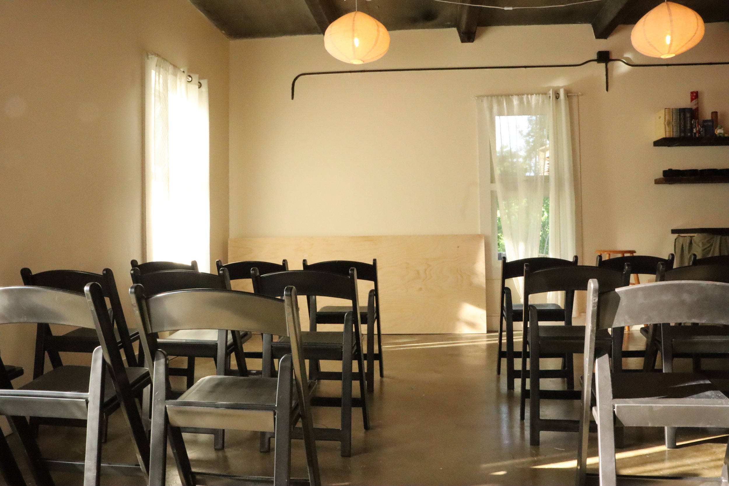 Empty chairs arranged in rows inside a room with large windows and hanging paper lantern lights.