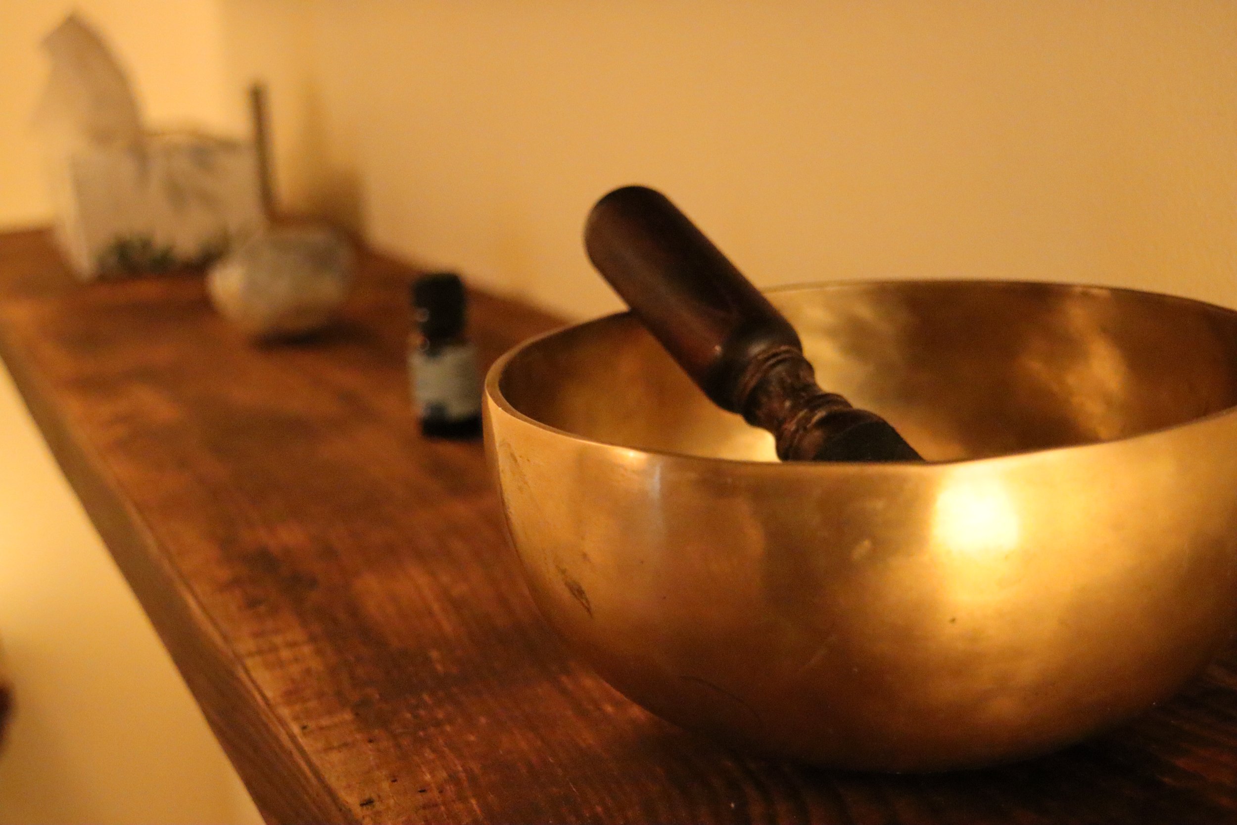 Bronze singing bowl with a wooden mallet resting inside, placed on a wooden surface.
