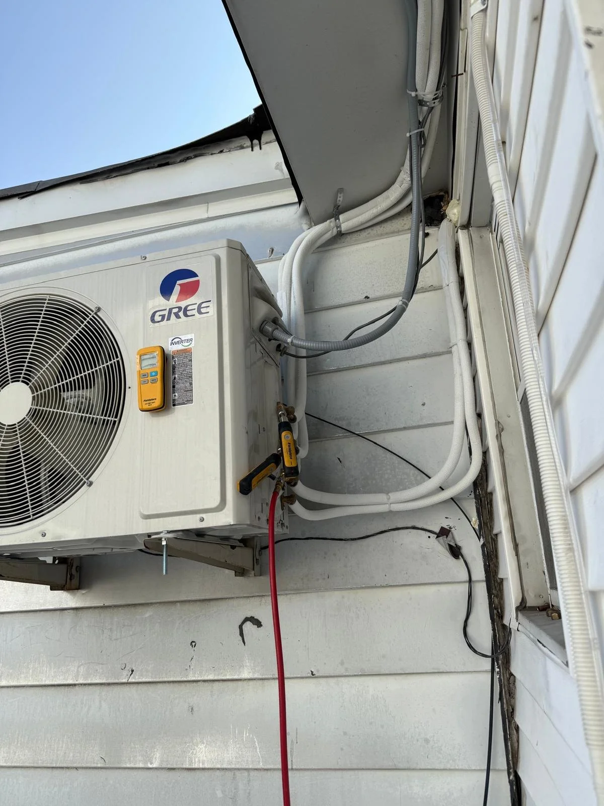 Close-up of an outdoor air conditioning unit on a house wall, with electrical and refrigerant lines connected.