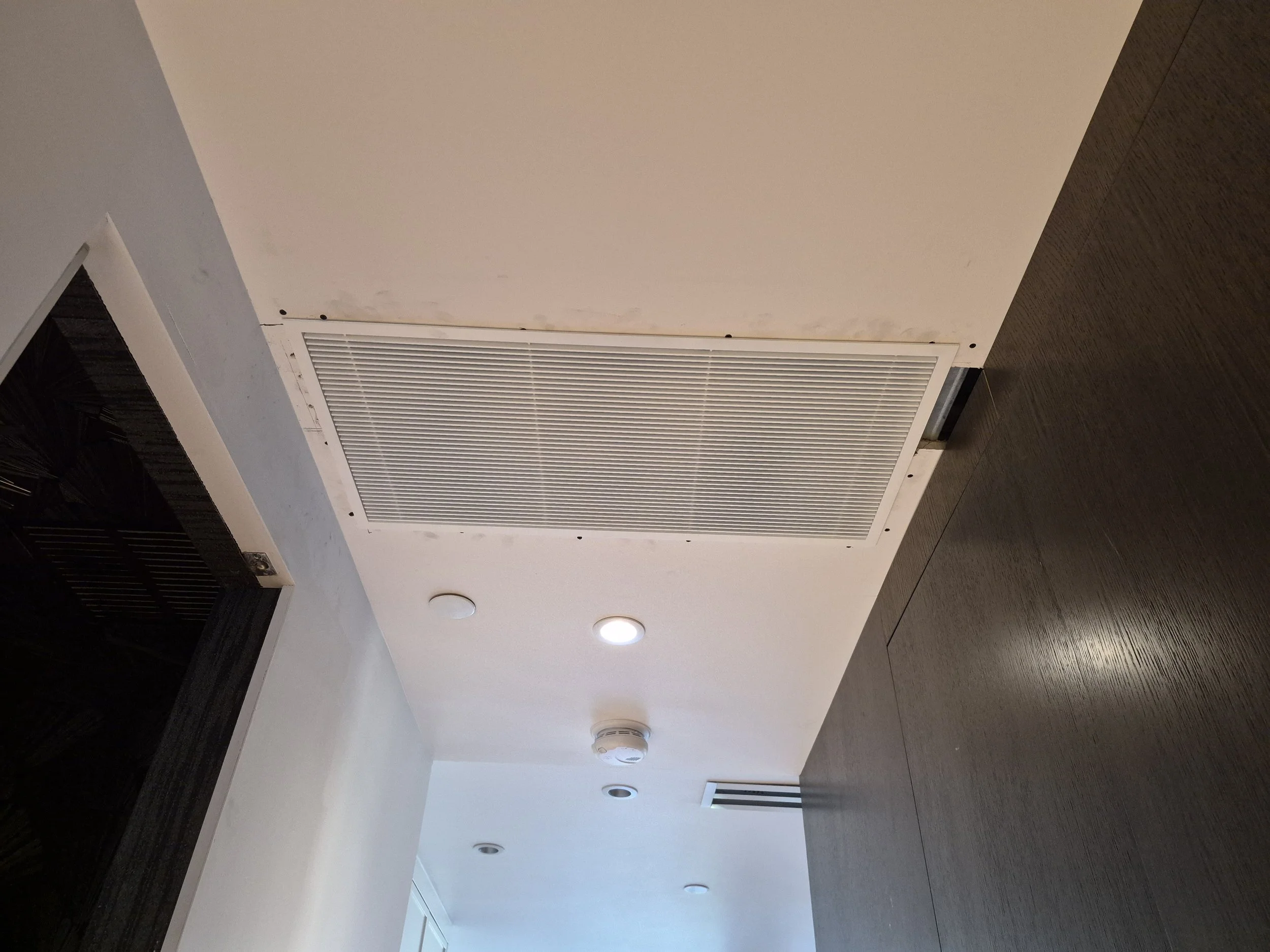Ceiling with white vent, smoke detector, and several recessed lights in a modern interior.