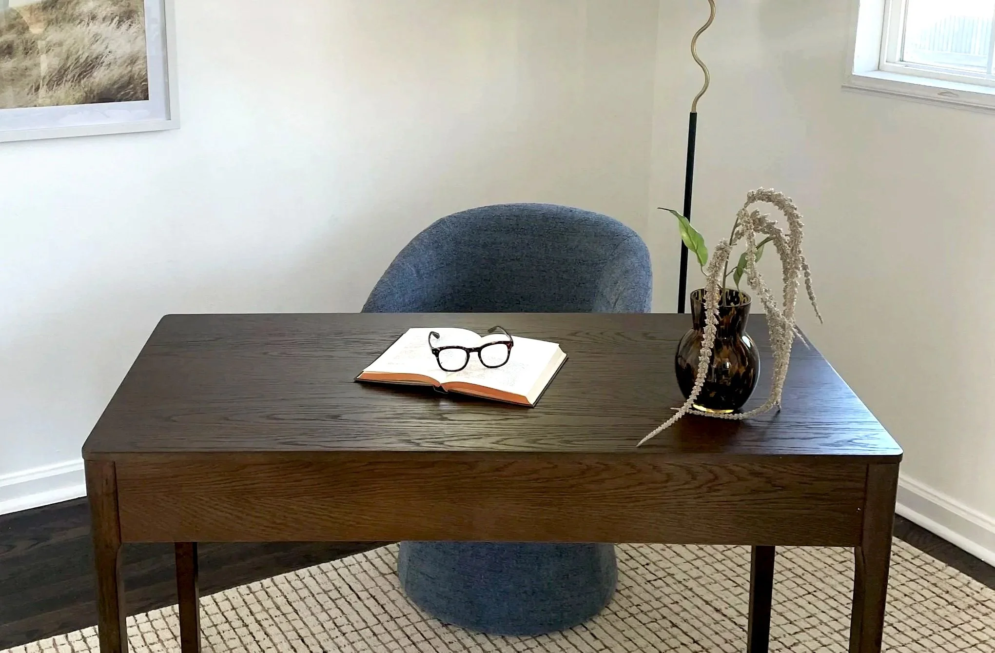 A kitty-cornered desk with a book and reading glasses on top of the book.