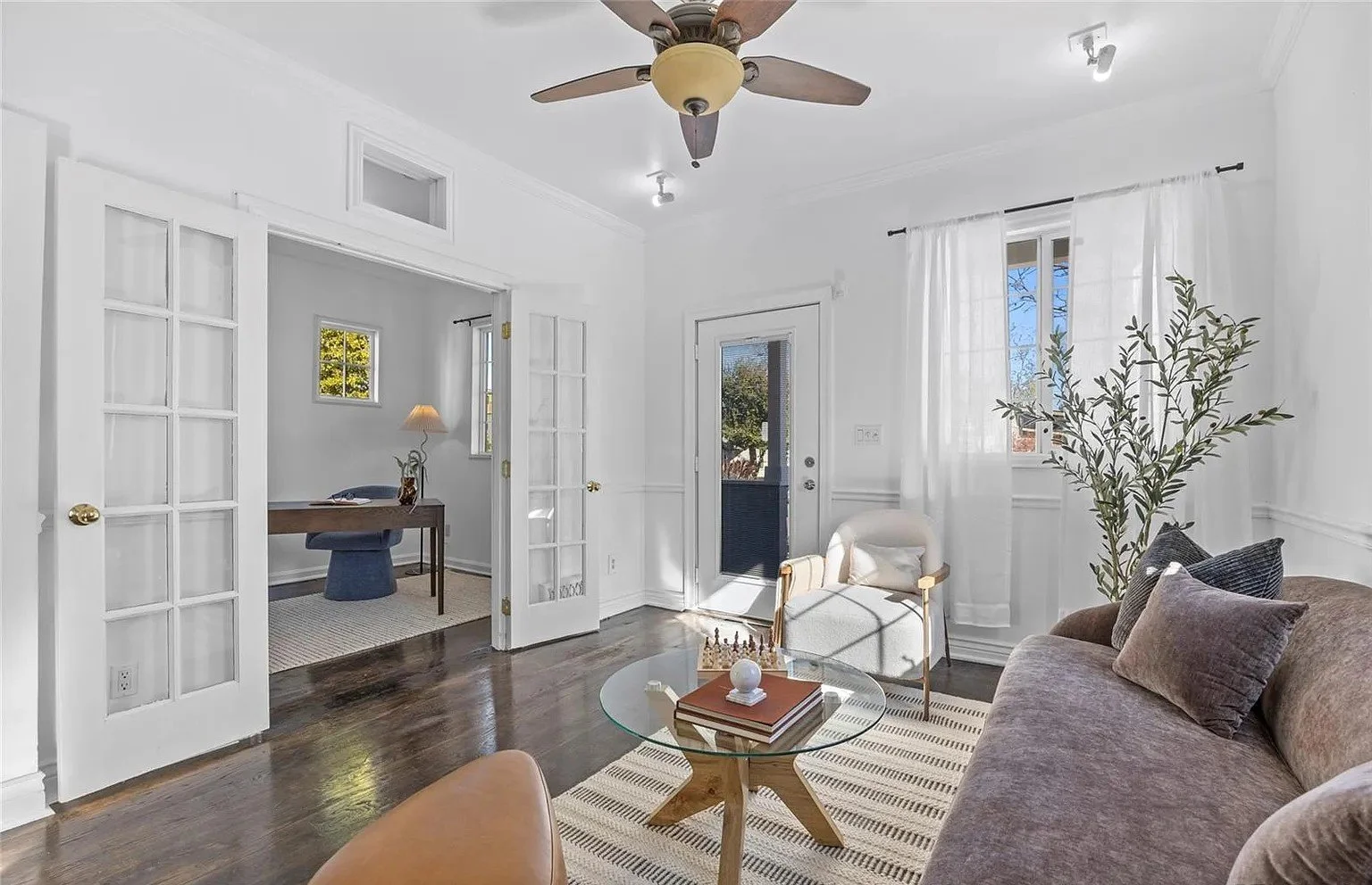 A light, airy living room with a velvet chocolate couch, round glass table, plants and a cozy white lounge chair.