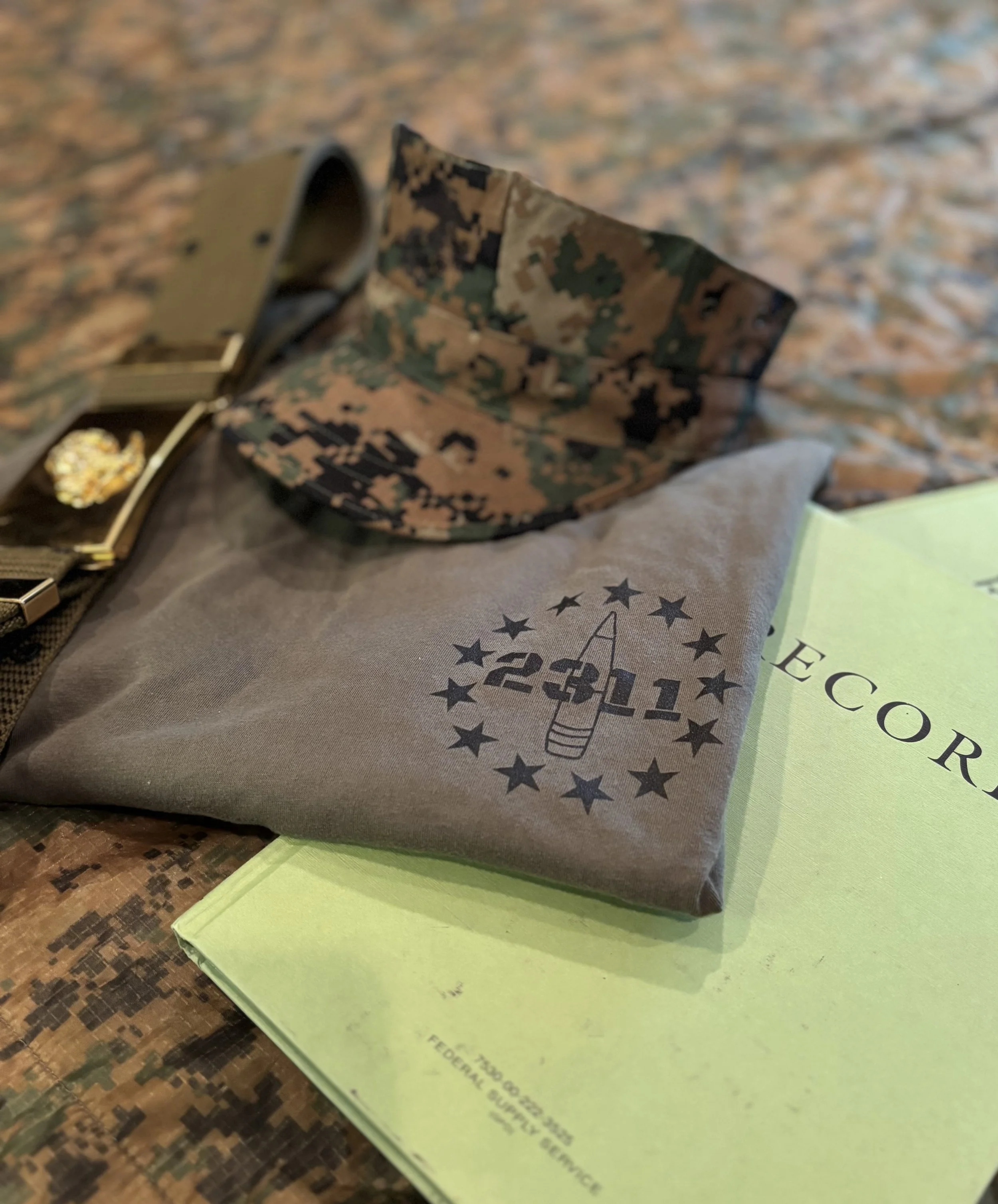 A gray cloth with a 2021 election-themed logo, a camouflage face mask, and a green document titled 'ELECTION' on a wooden surface.