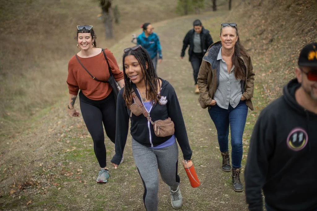 Group of people hiking on a dirt trail in a wooded area.