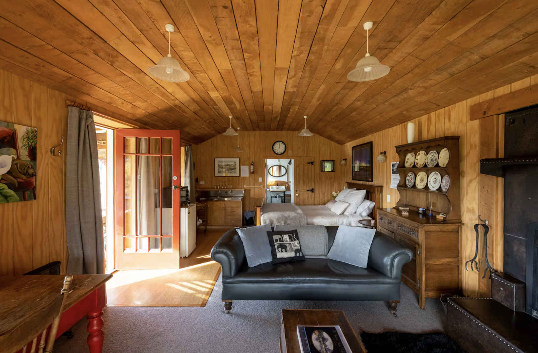 Wood-paneled living room with leather sofa, wooden furniture, and a wood ceiling, leading to a bedroom and a bathroom.