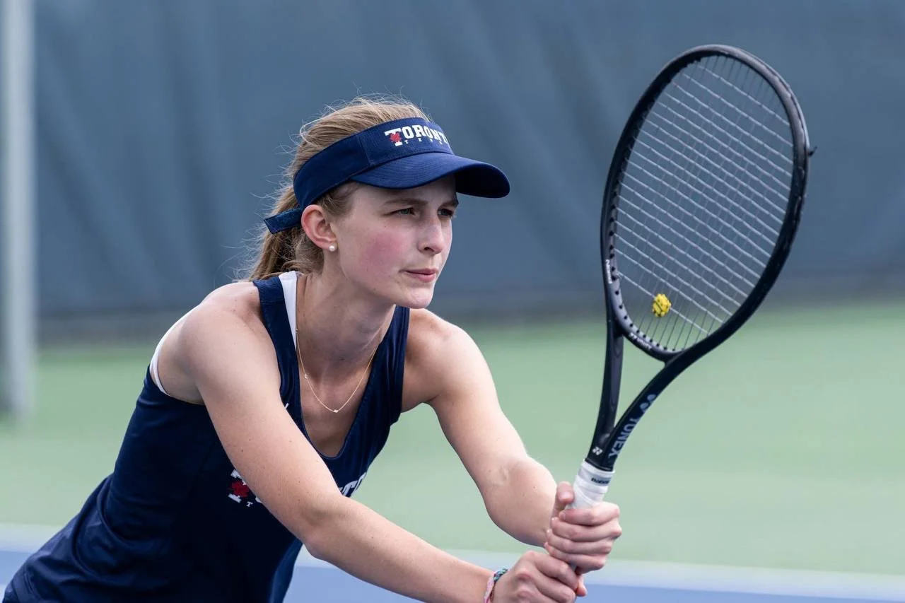 Young woman in a navy sports outfit and visor holding a tennis racket on a tennis court.