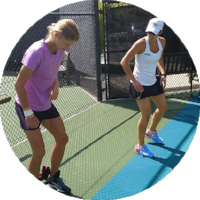 Two women are on a green tennis court, practicing with a blue agility ladder. One is wearing a purple shirt and black shorts, and the other is in a white tank top and black shorts.