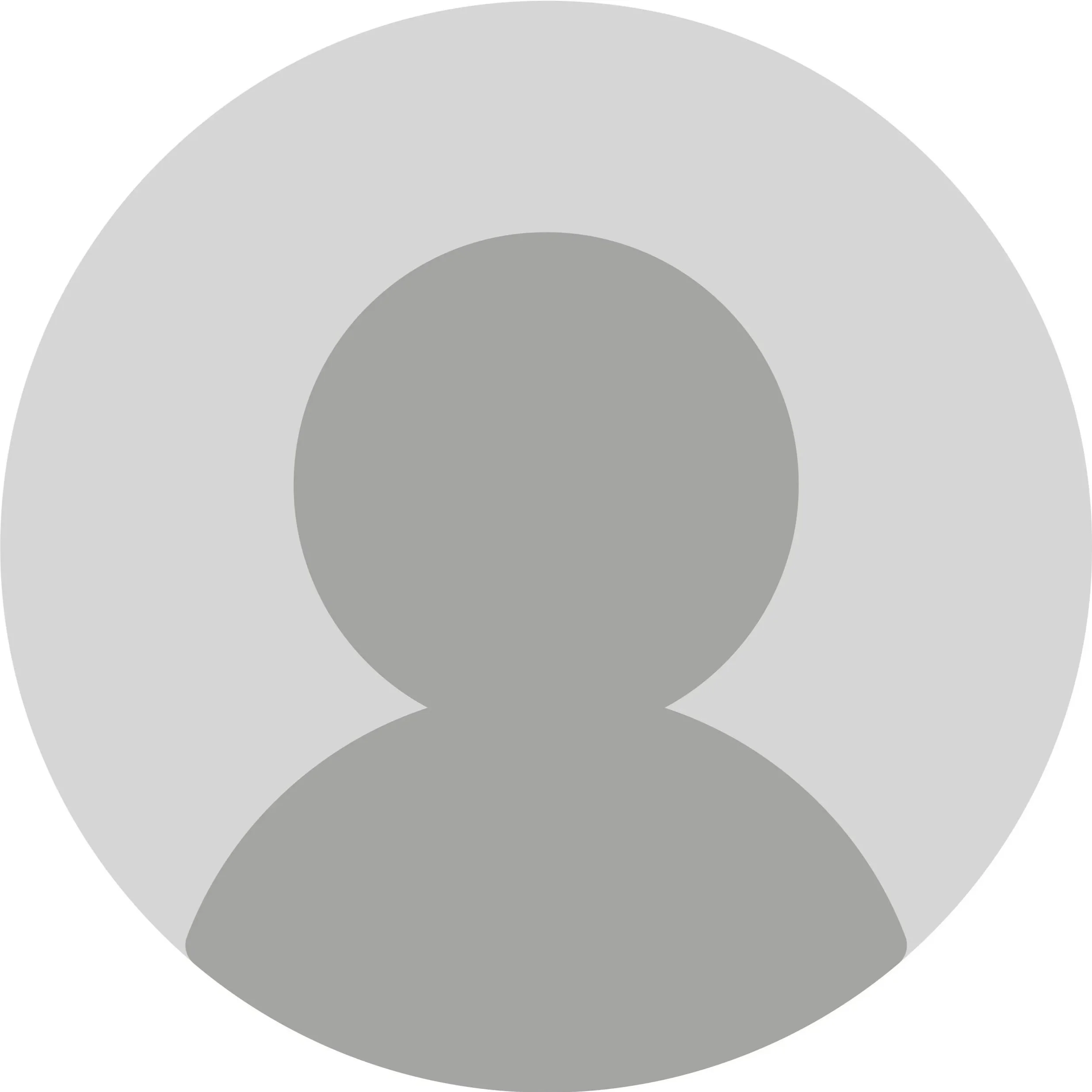 A man with glasses, a nose ring, and a beard, wearing a black sweater, sitting indoors near a plant, smiling softly.