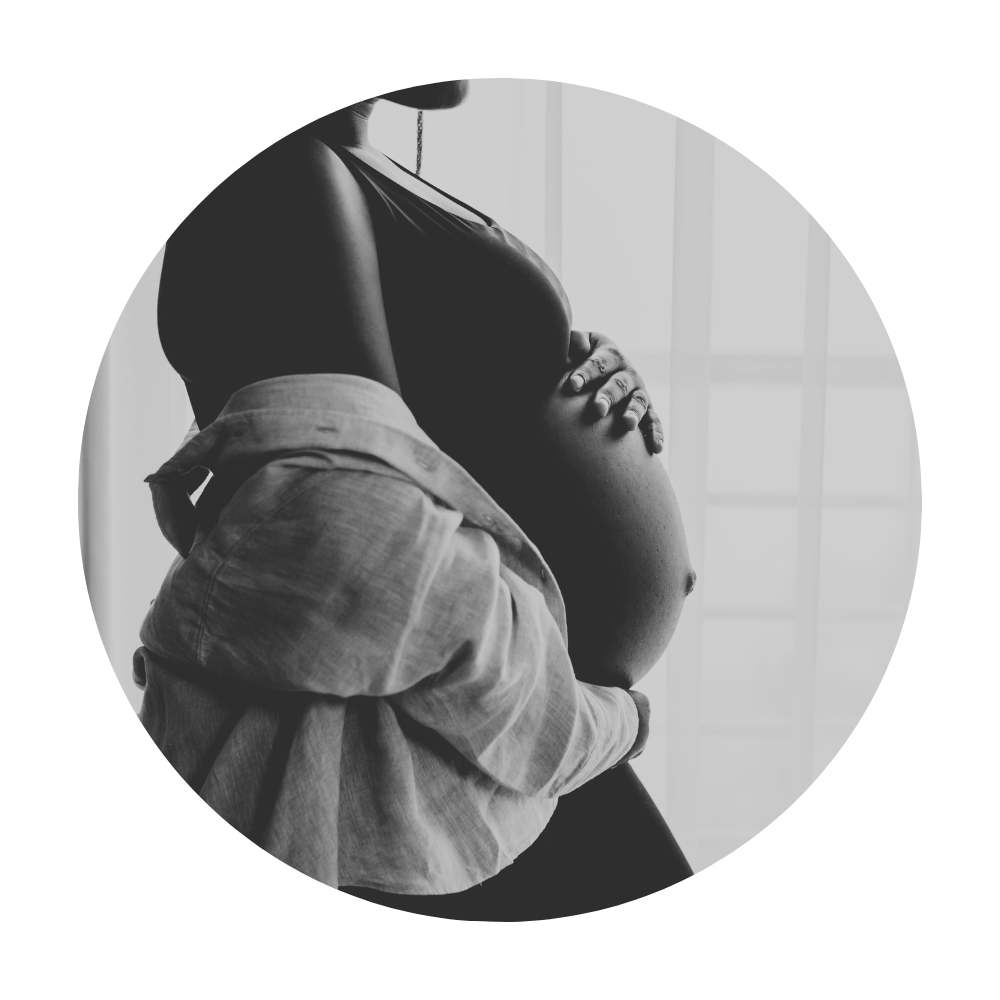 A pregnant woman with a bare belly, seen from the side, being gently cradled by another person.