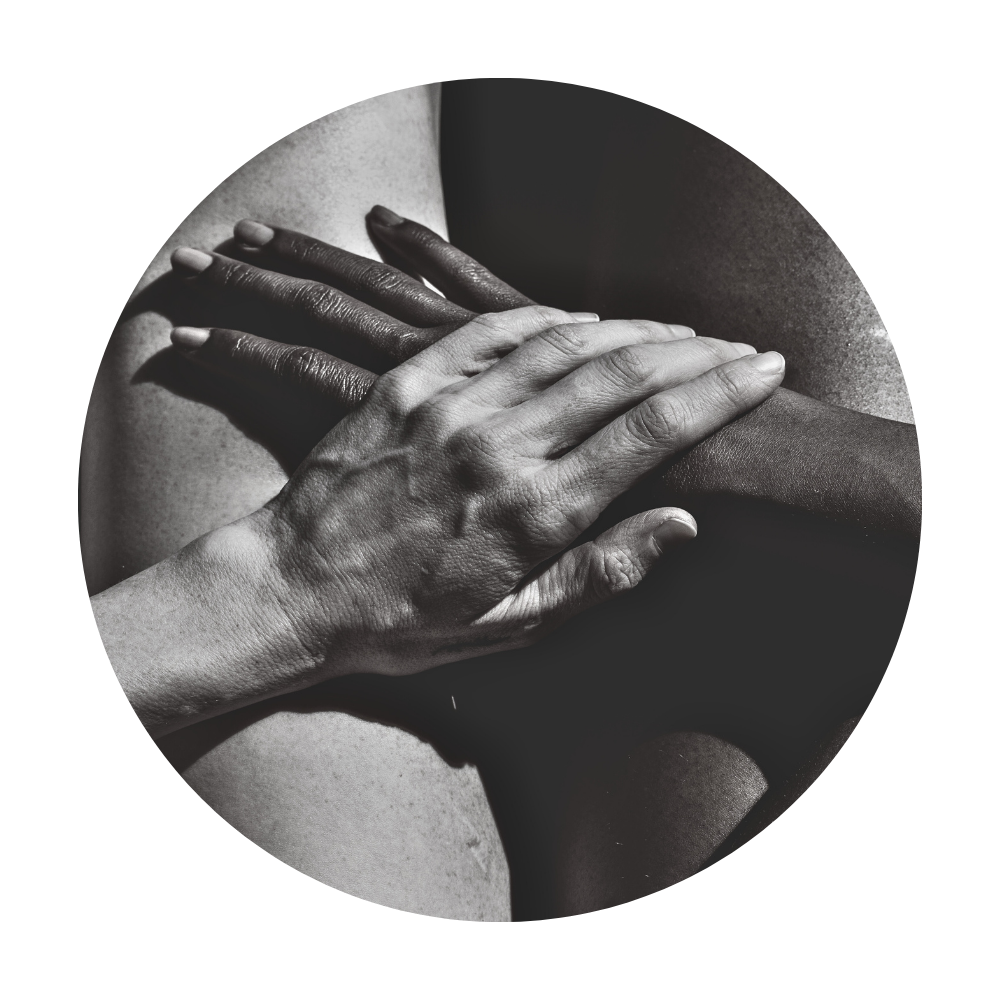 Black and white close-up of one person gently holding the hand of another person with different skin tones, emphasizing human connection and care.