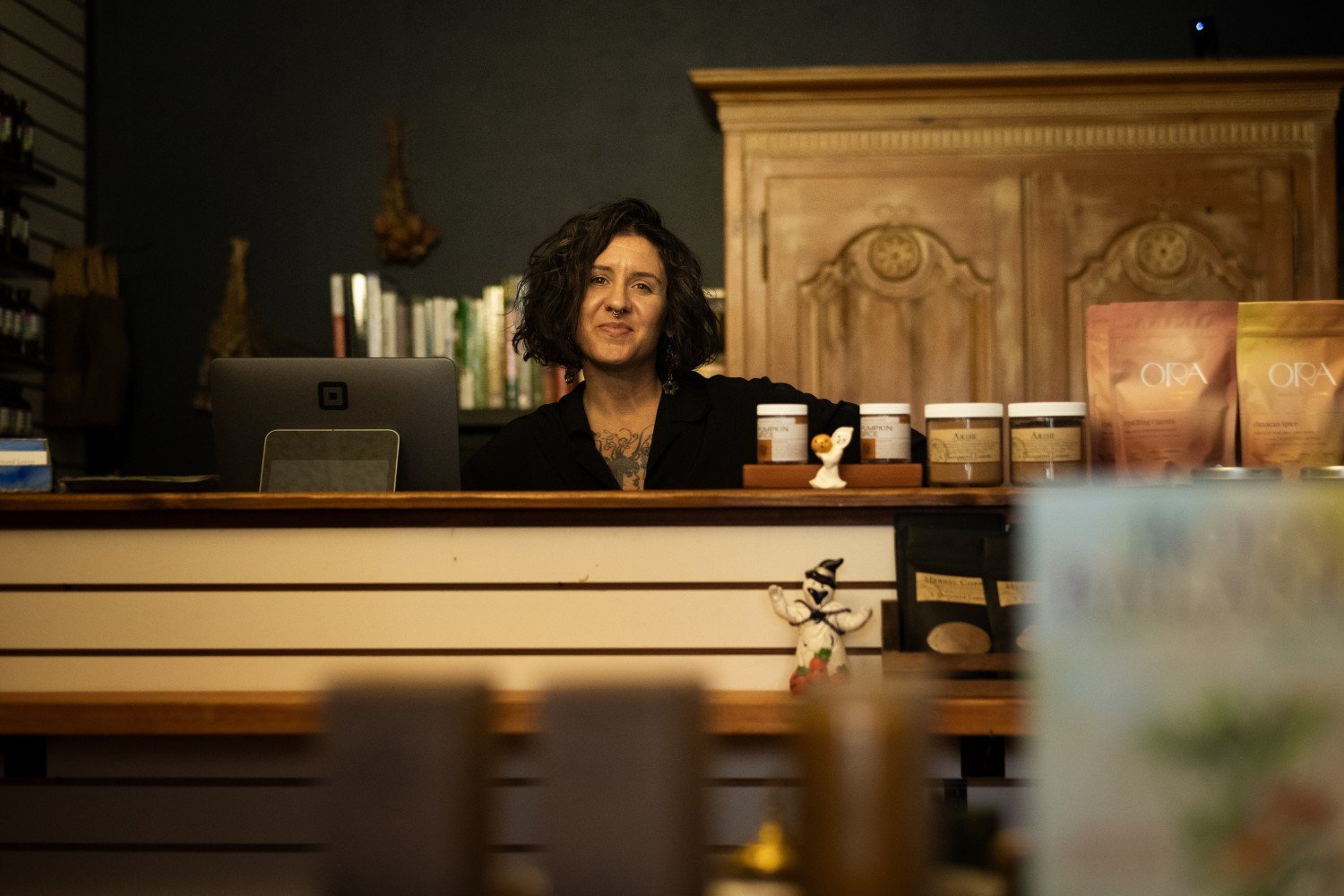 A woman with short dark hair and black blouse standing behind a shop counter and smiling at the camera.