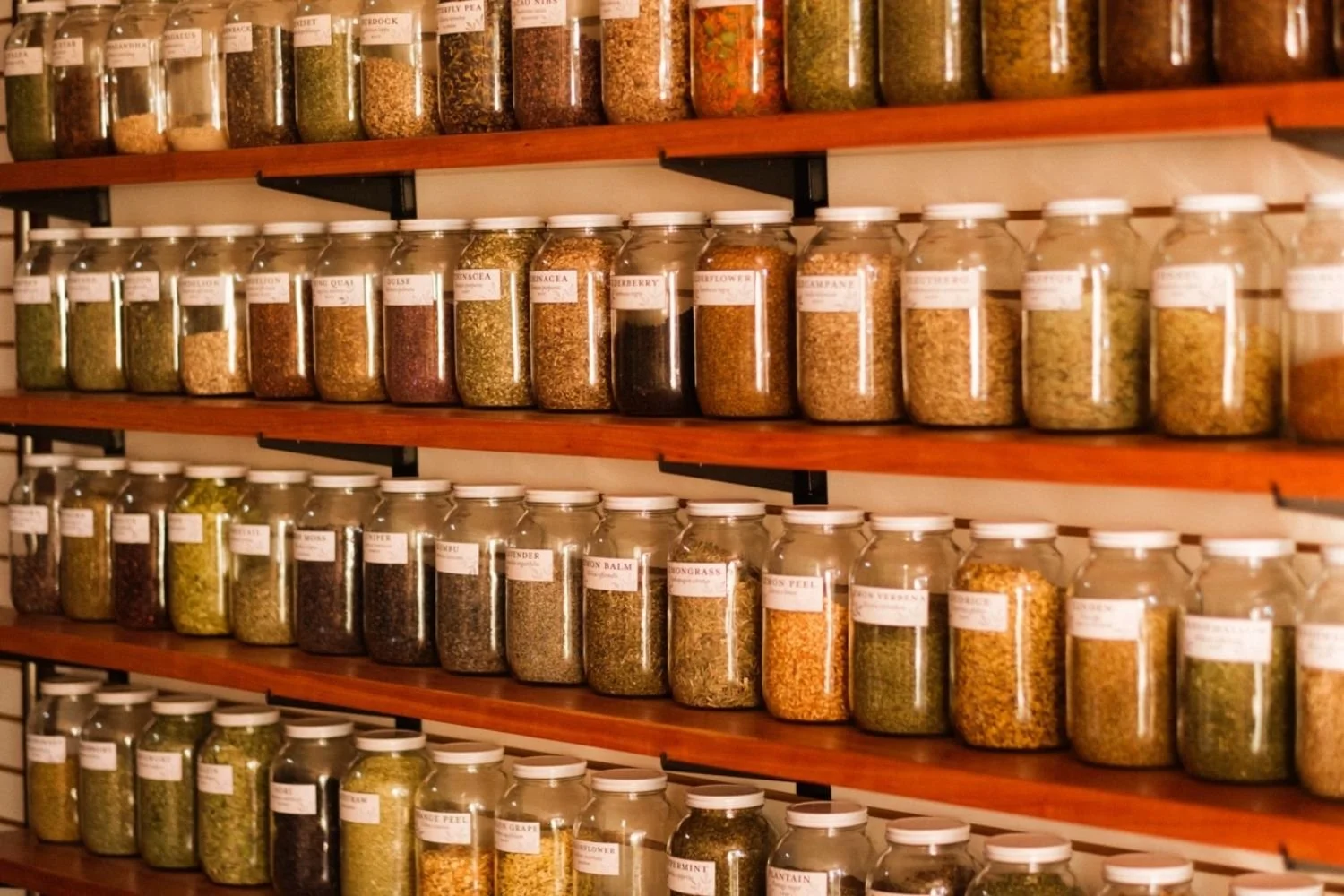 An angled view of a wall with shelves lined with large jars filled with loose herbs.