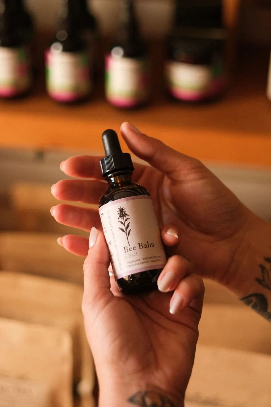 Two hands displaying a brown dropper bottle labeled as Bee Balm