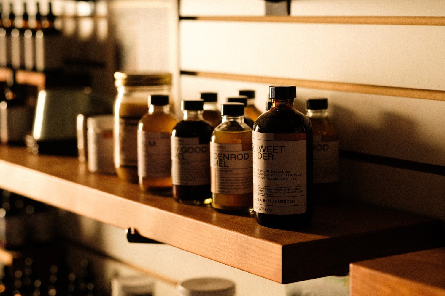 A variety of bottles lined up on a shelf in mostly shadow.