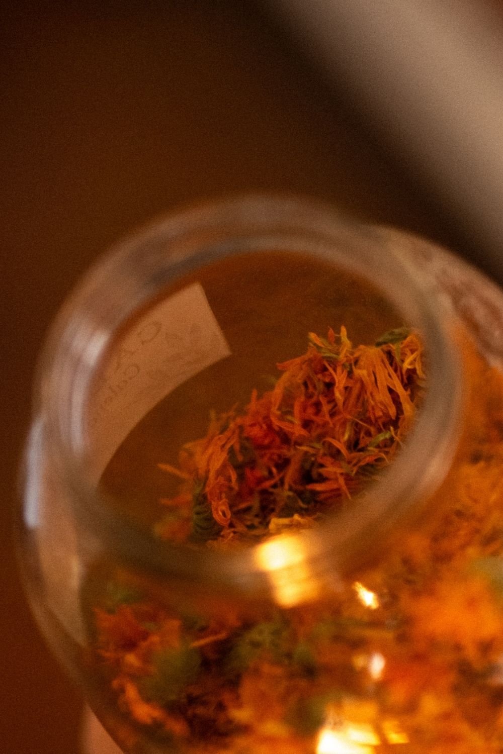 Close up looking down into an open jar of redish orange dried flower petals.