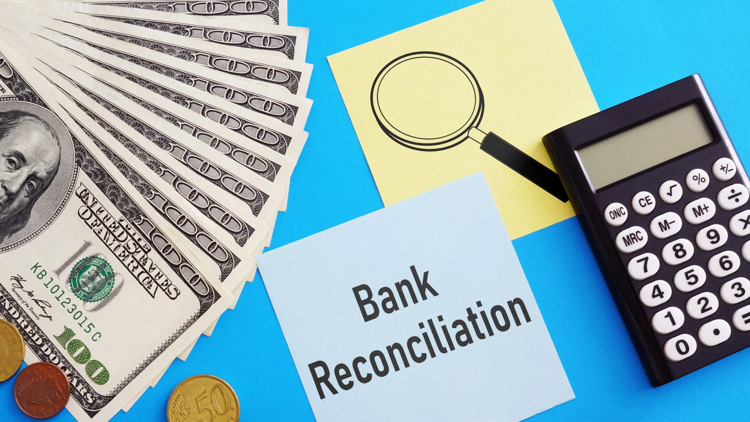 U.S. hundred-dollar bills fanned out, various coins, a calculator, and a paper with "Bank Reconciliation" written on it on a blue background, with a yellow note featuring a magnifying glass drawing.