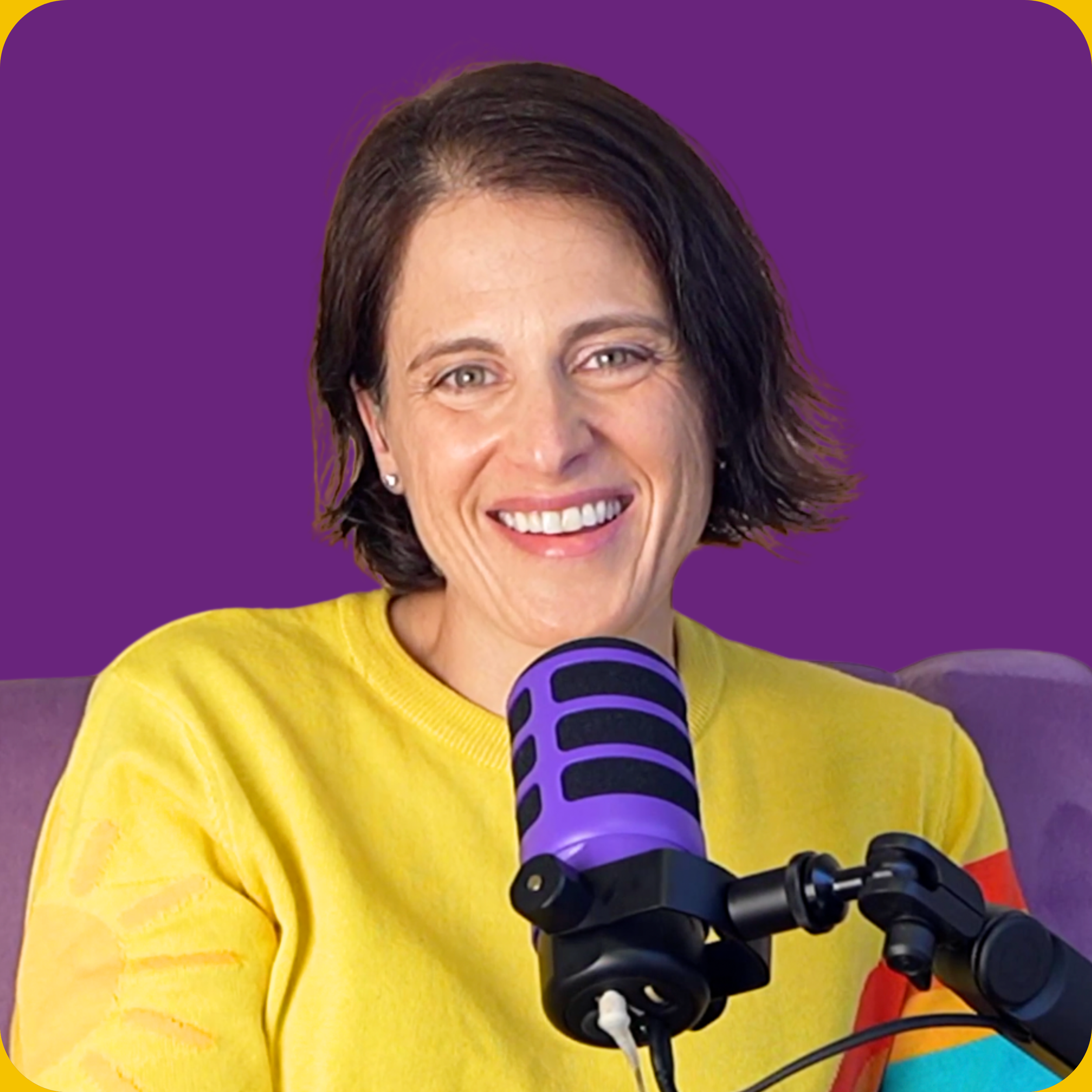 A woman with short dark hair, wearing a yellow shirt, smiling in front of a purple background, sitting in front of a purple microphone.