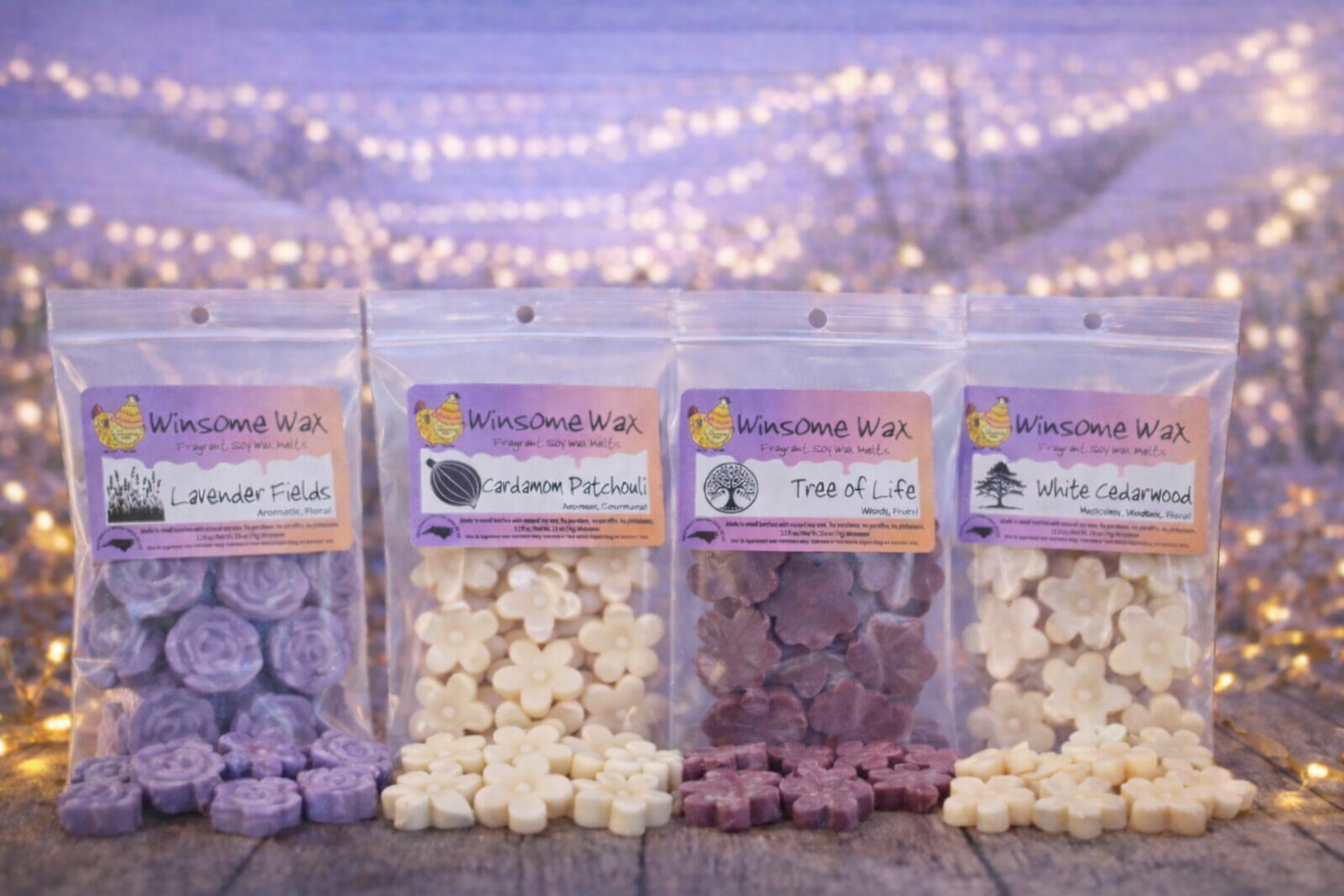Four packets of wax melts labeled Lavender Fields, Cardamom Patchouli, Tree of Life, and White Cedarwood, arranged on a wooden surface with a blurred background of fairy lights.