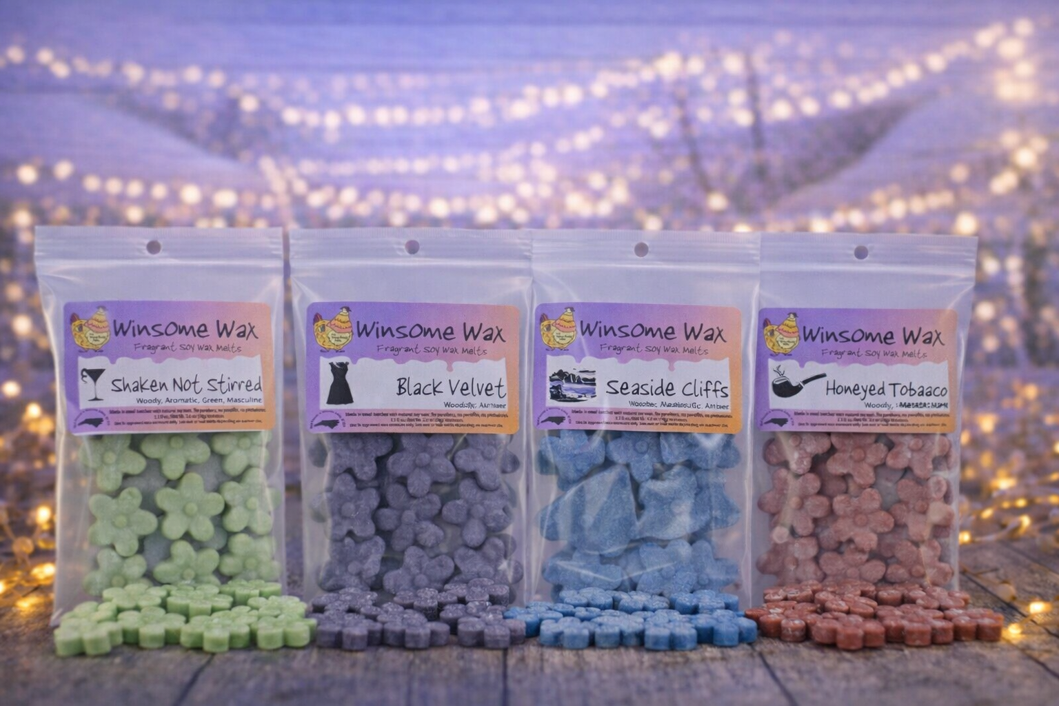 Four packets of Winsome Wax fragrant soy wax melts on a wooden surface, each with different scents and pastel-colored wax melts, against a blurred background of string lights.