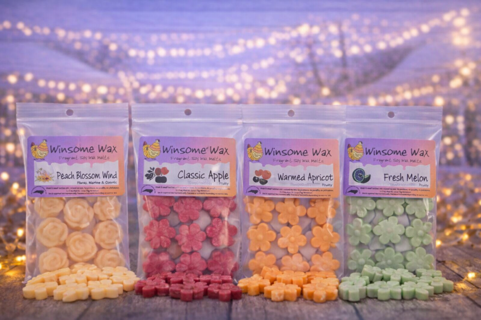 Four packages of Winsome Wax fragrant soy wax melts in peach blossom wind, classic apple, warmed apricot, and fresh melon flavors, arranged on a wooden surface with fairy lights in the background.