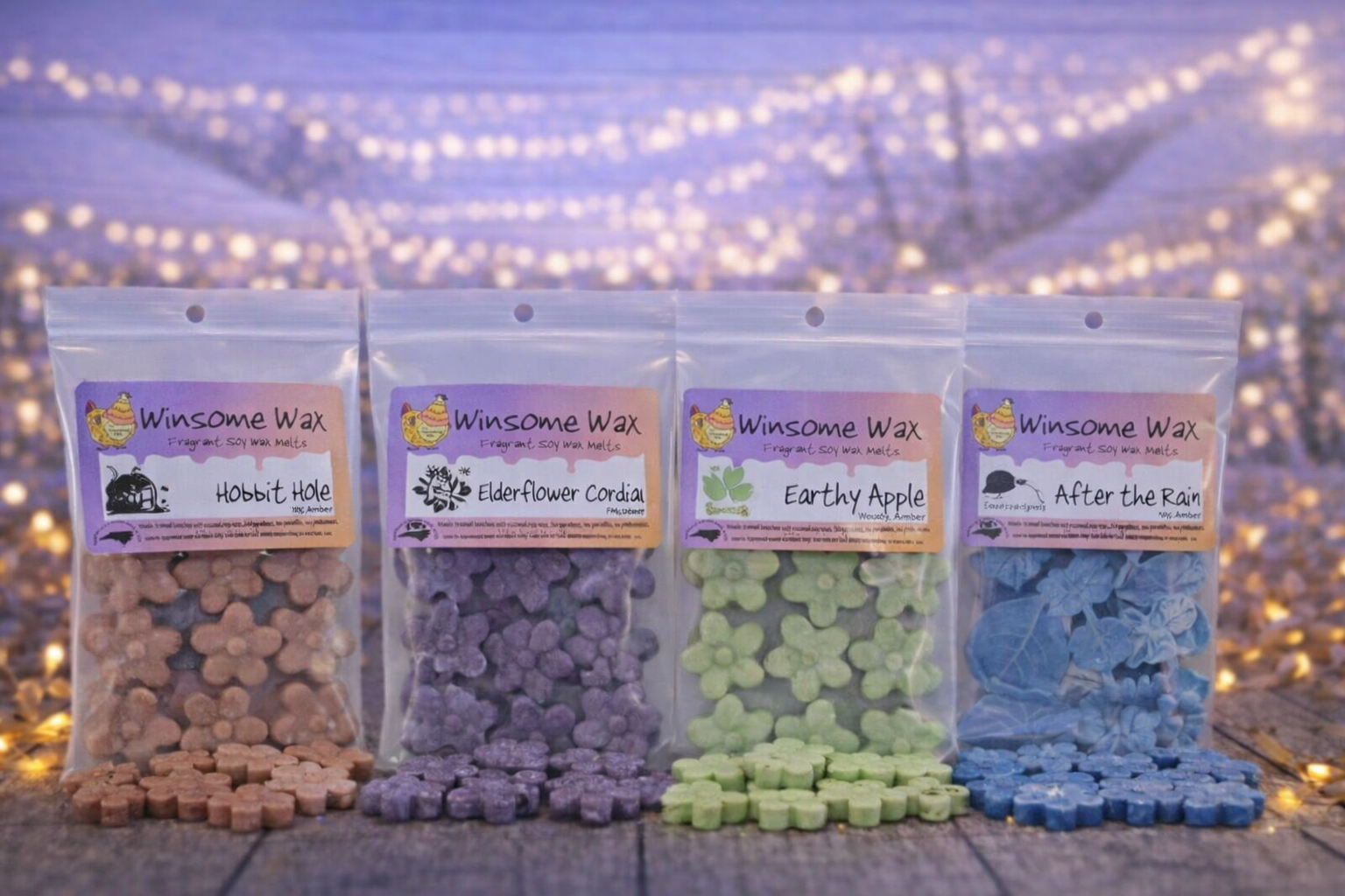 Four packages of Winsome Wax fragrant soy wax melts with different scents, arranged in a row on a wooden surface, with fairy lights in the background.