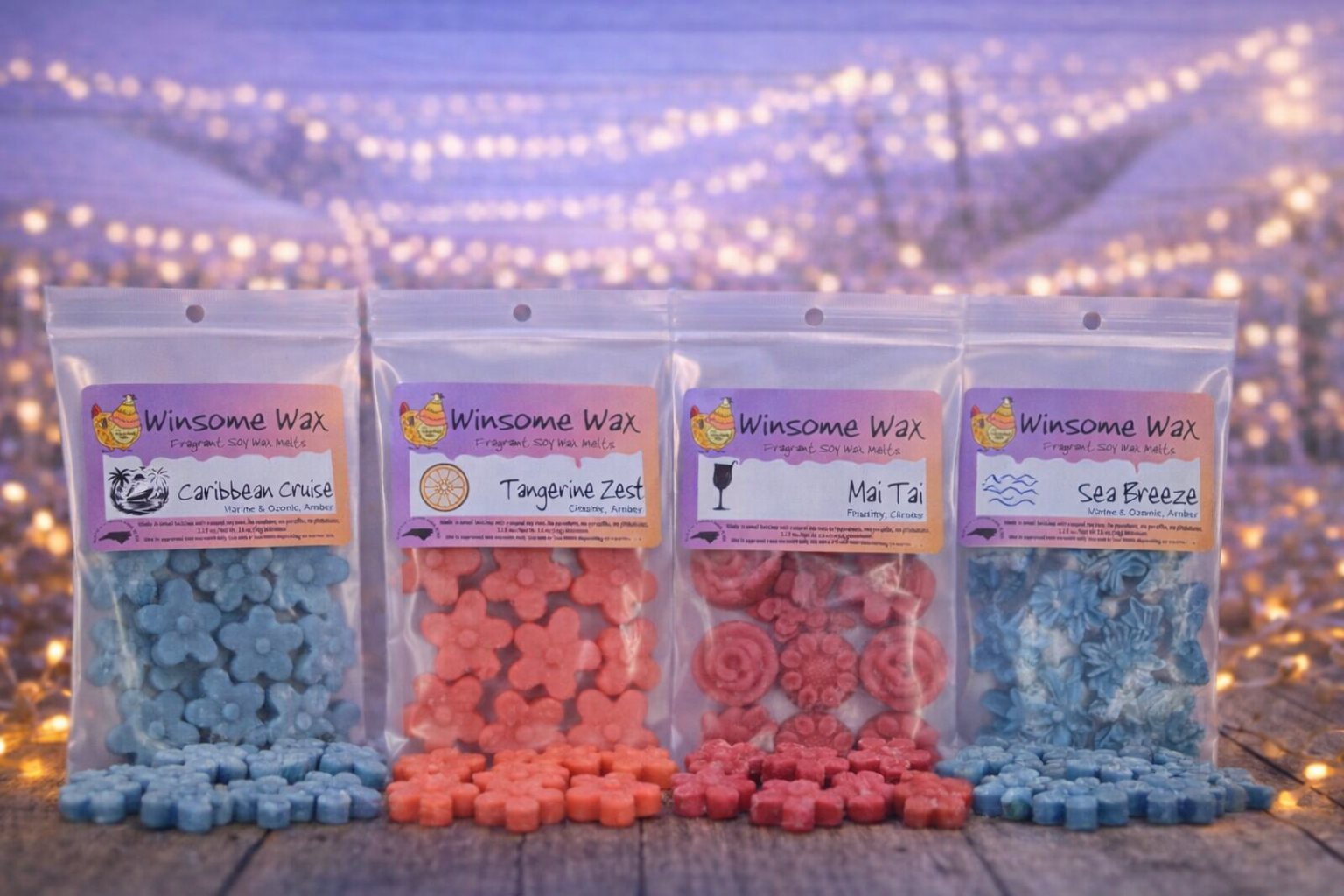 Four small resealable bags of colorful wax melts labeled with different tropical-themed names, arranged on a wooden surface at dusk with string lights in the background.