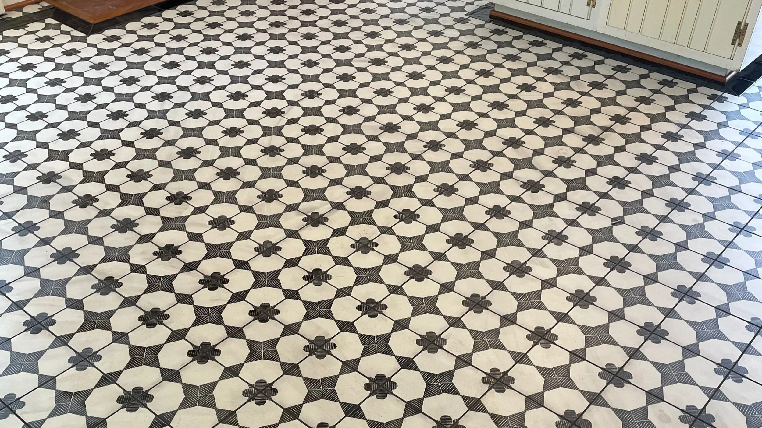 Black and white patterned tile floor with a geometric design of hexagons and small black bee motifs.
