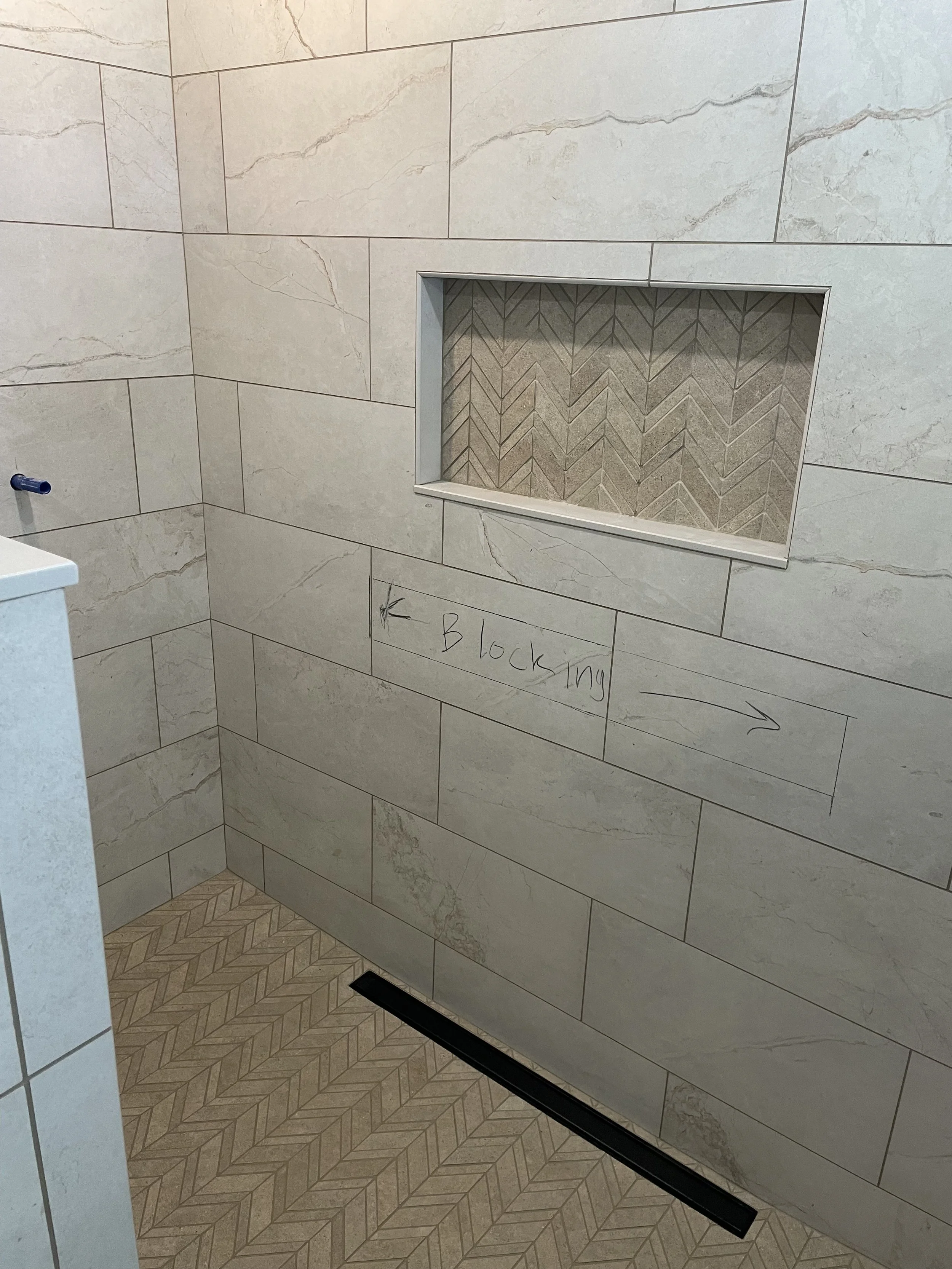 A bathroom shower wall with beige tiles, a built-in niche with herringbone pattern tiles, and a note with an arrow pointing right that says 'Blocking'.