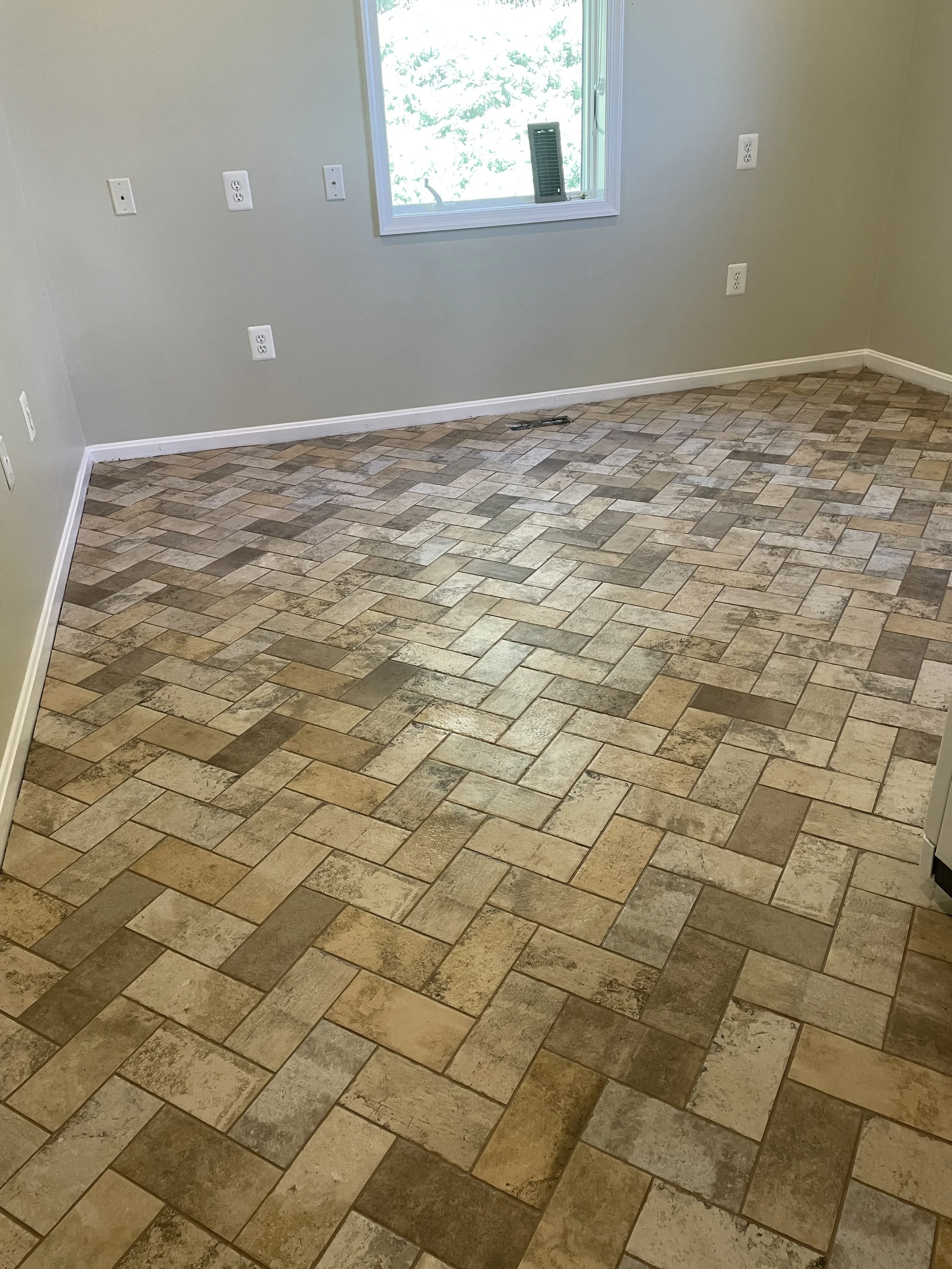 Empty room with beige tiled floor, light green walls, a window with a white frame, and multiple electrical outlets.