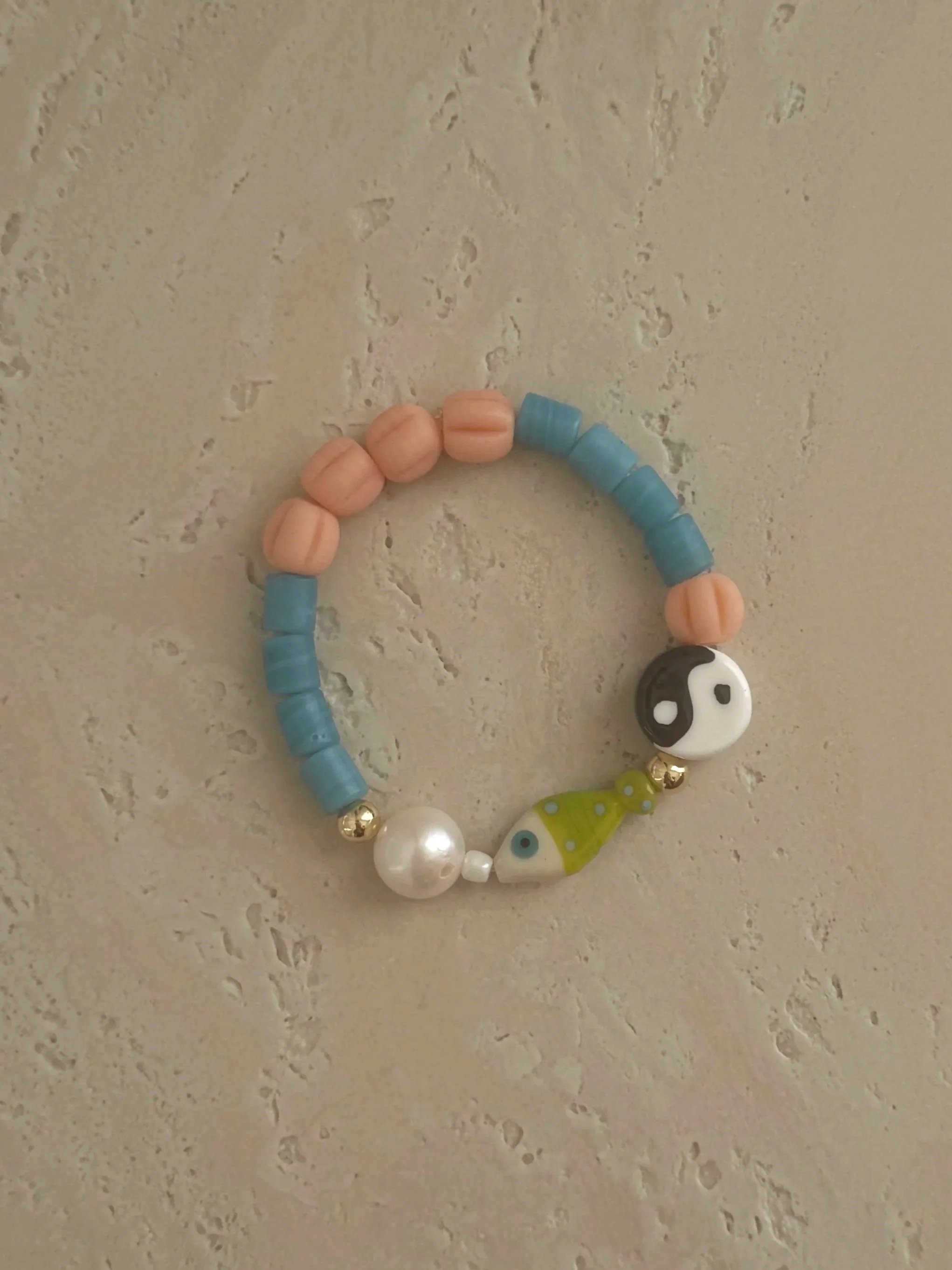 Handmade ÒNDE bracelet with blue and peach beads, freshwater pearl and glass fish charm