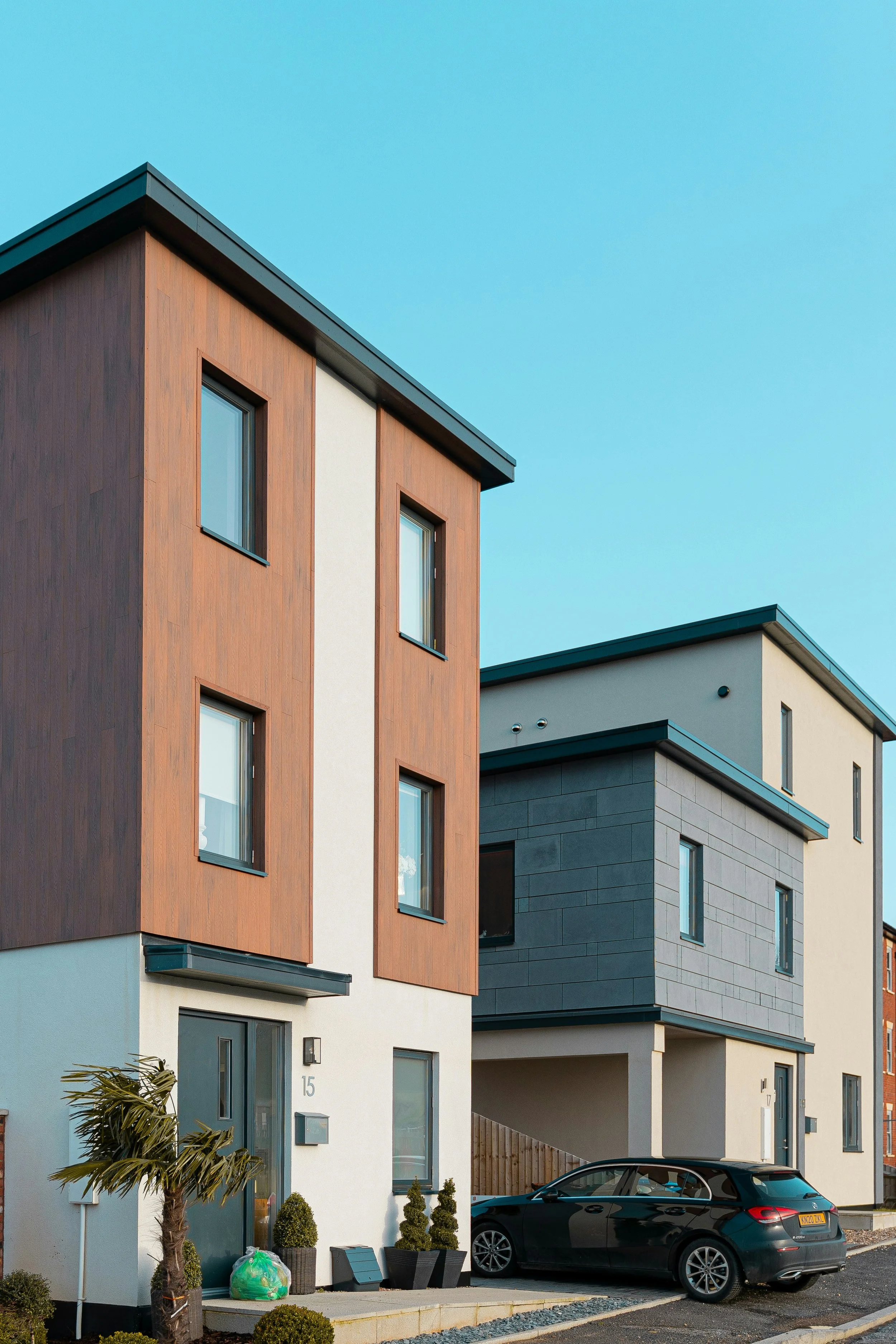 Modern multi-story residential buildings with sleek design, large windows, and parked black car in front.