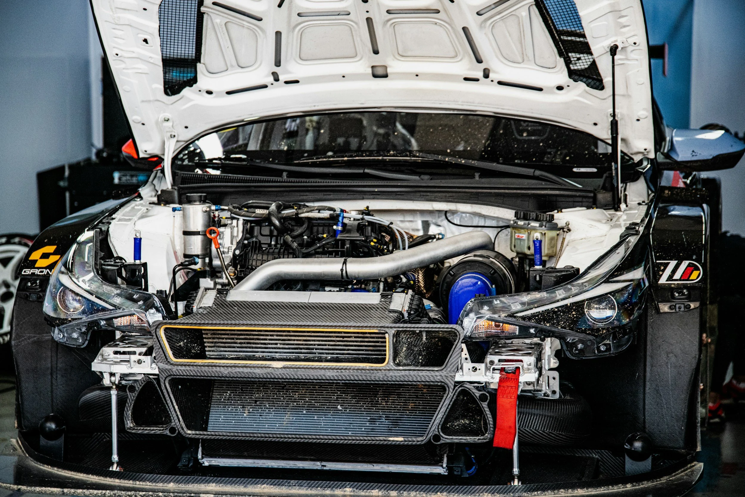 Front view of a car with its hood open, showing the engine and various mechanical components, including a large intercooler, pipes, and wiring.