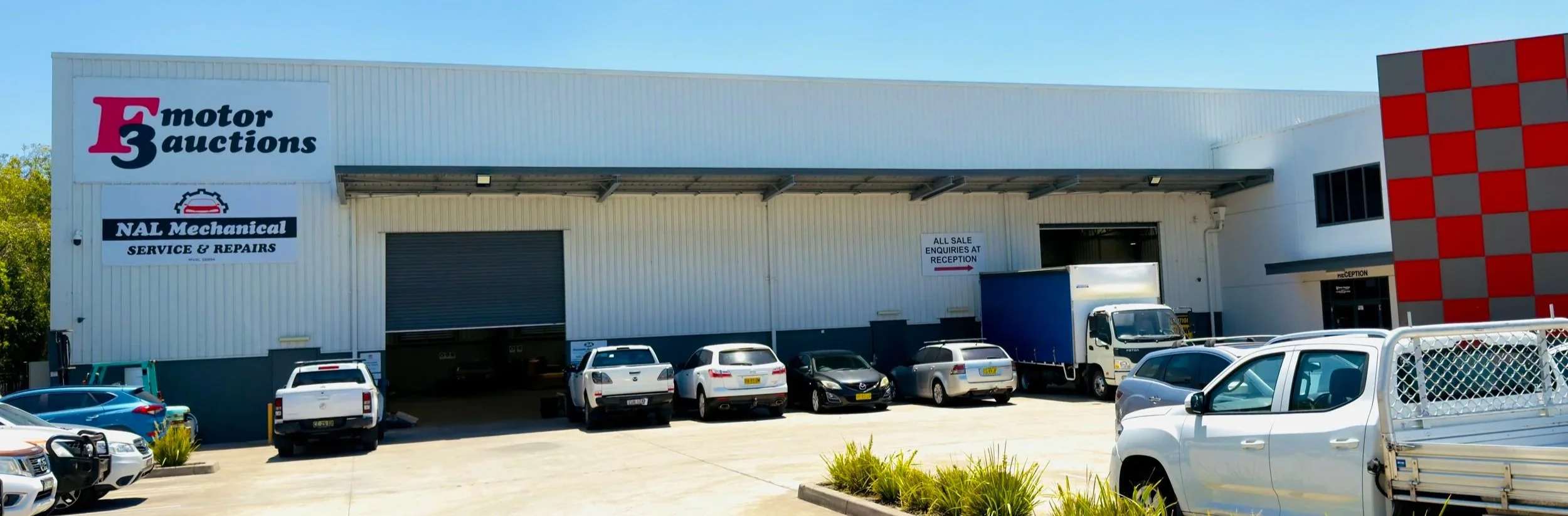 Exterior of NAL Machanical, with several parked cars and a delivery truck in front. There are signs indicating service, repairs, and reception.