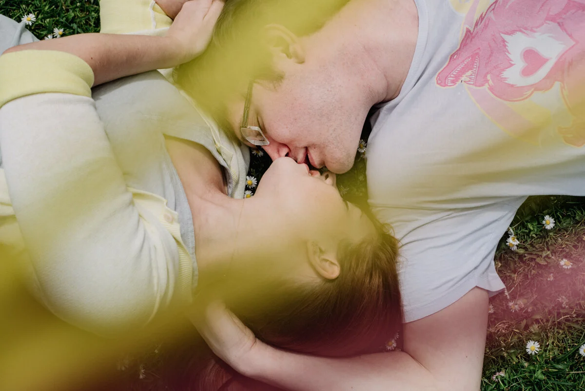 A man and a woman lying on the grass, kissing, with flowers surrounding them.