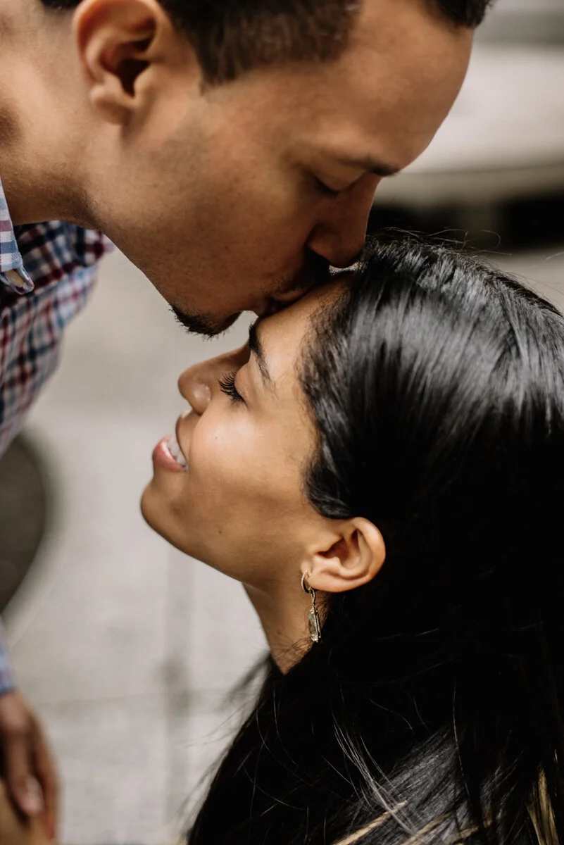 A man leaning in to kiss a woman on the forehead, both smiling and appearing affectionate.
