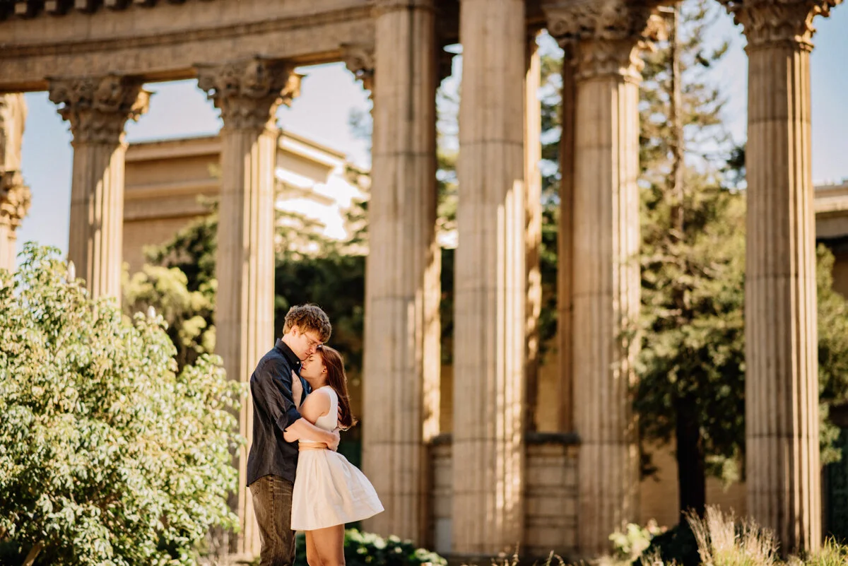 A young couple hugging under ancient Greek-style columns outdoors during daytime.