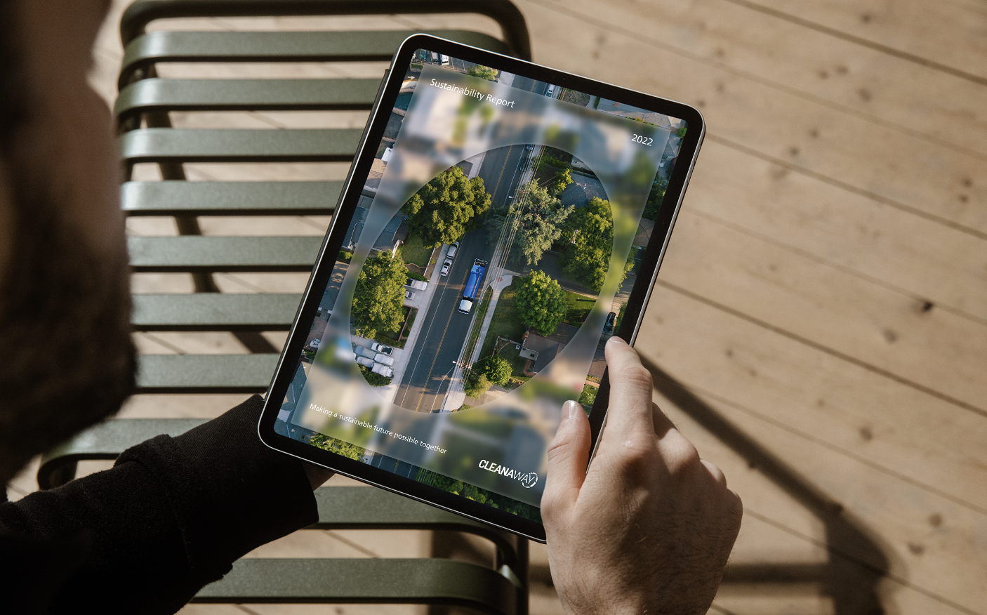 Person holding a tablet displaying a sustainability report with an aerial view of a green city street.