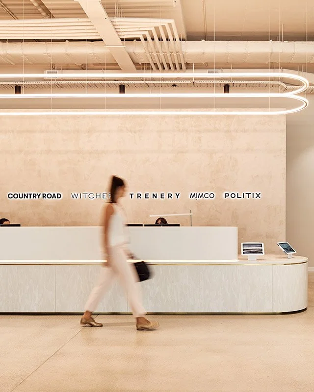 Modern reception area with a long counter, a woman walking in front, and minimal signage for country road, witcher, trenery, mimco, politix.